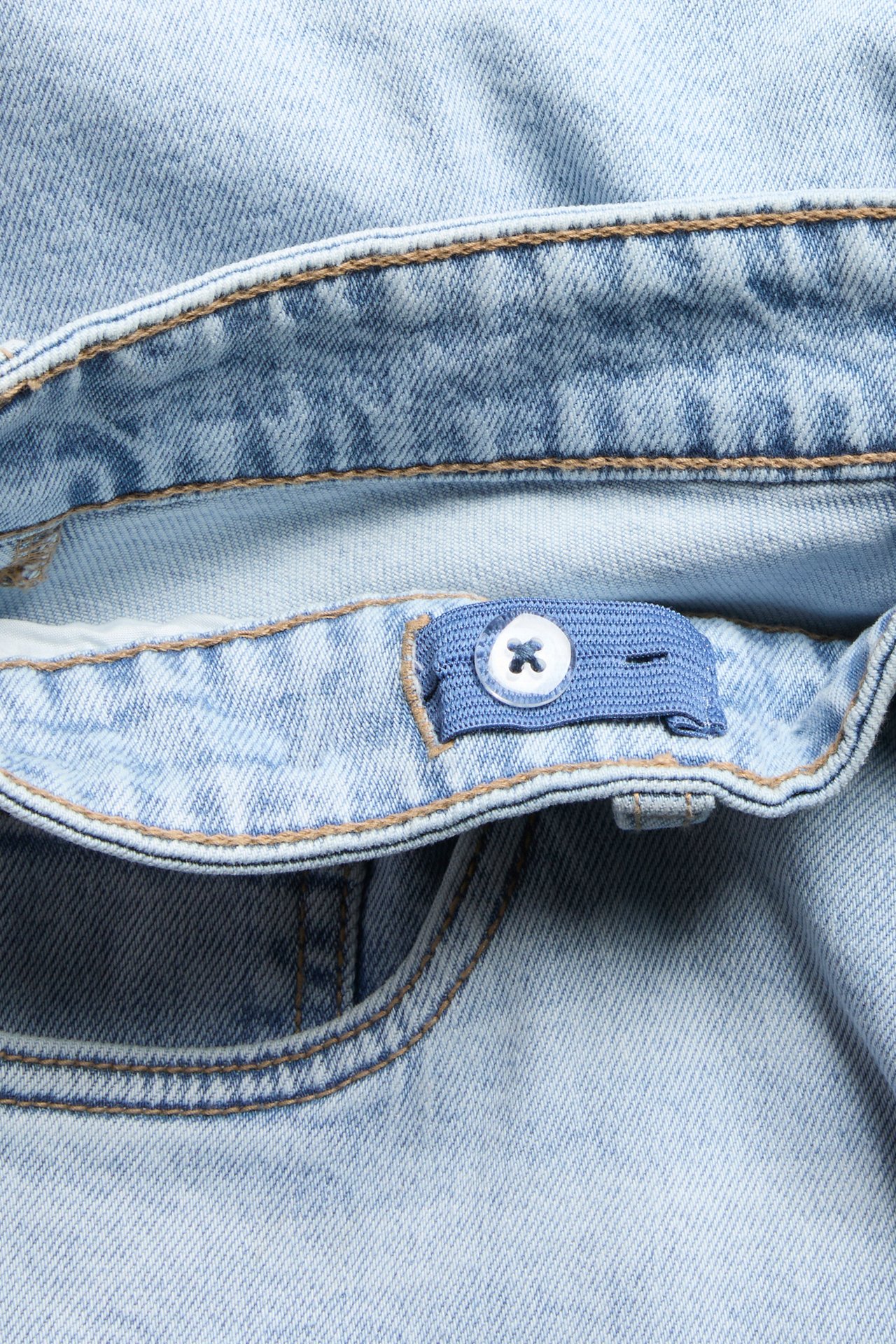 Nærbilde av lyseblå denimshorts med brune sømmer og justerbart liv med en hvit knapp.