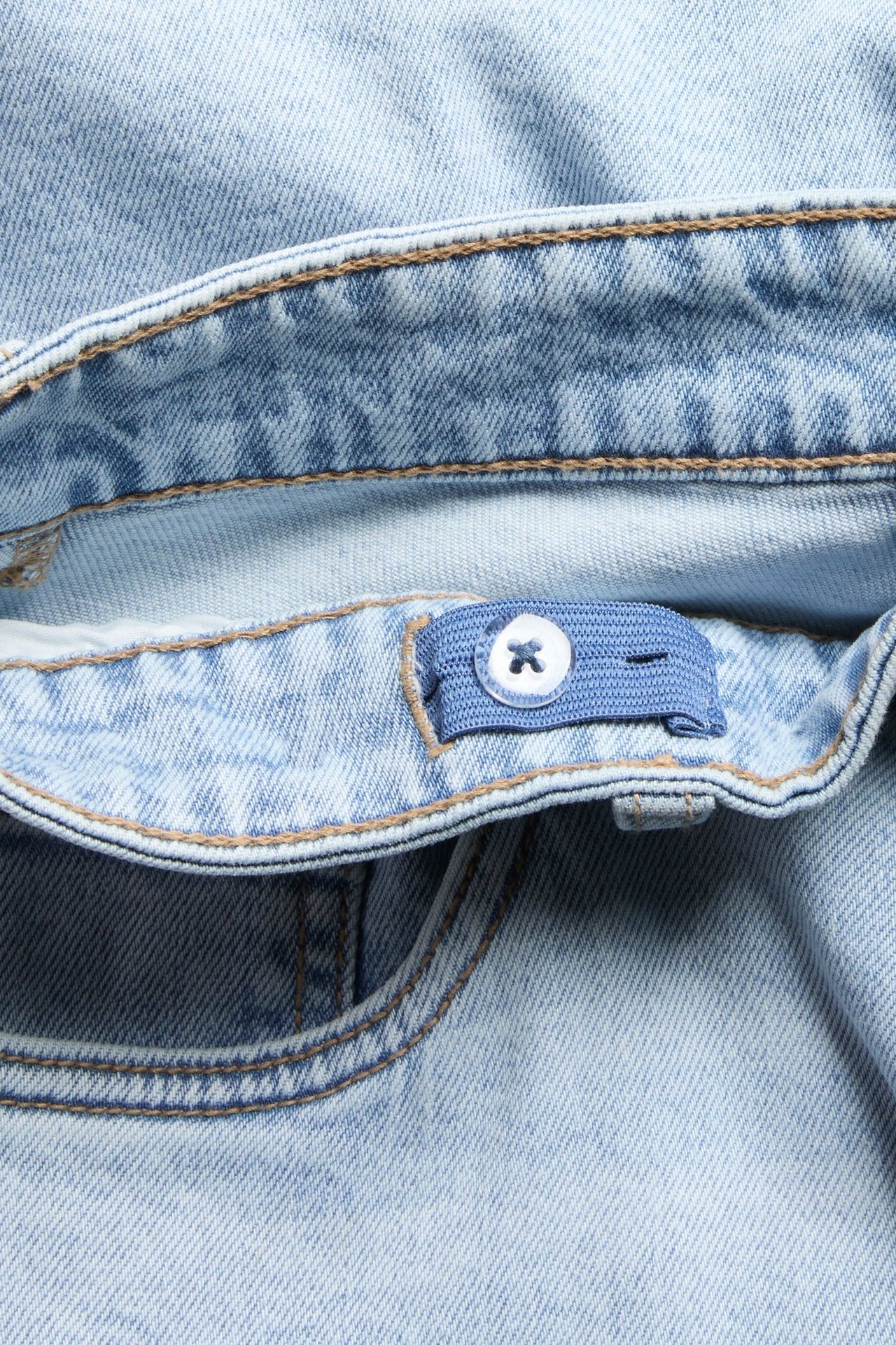 Zbliżenie na jasnoniebieskie szorty jeansowe z brązowymi szwami i regulowanym pasem z białym guzikiem.