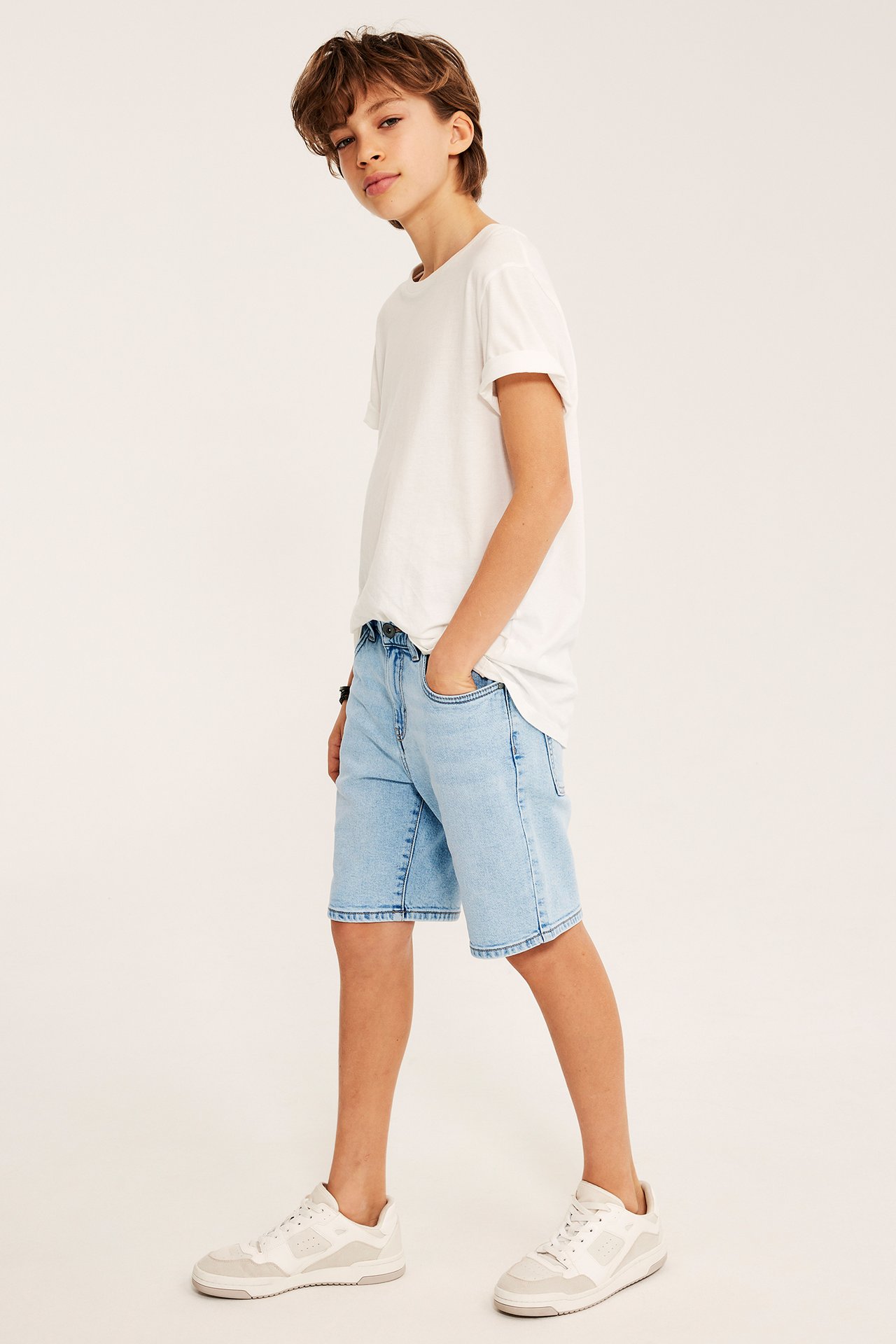 Sidovy av ett barn i ljusblå stretchjeansshorts, en vit t-shirt och vita sneakers.