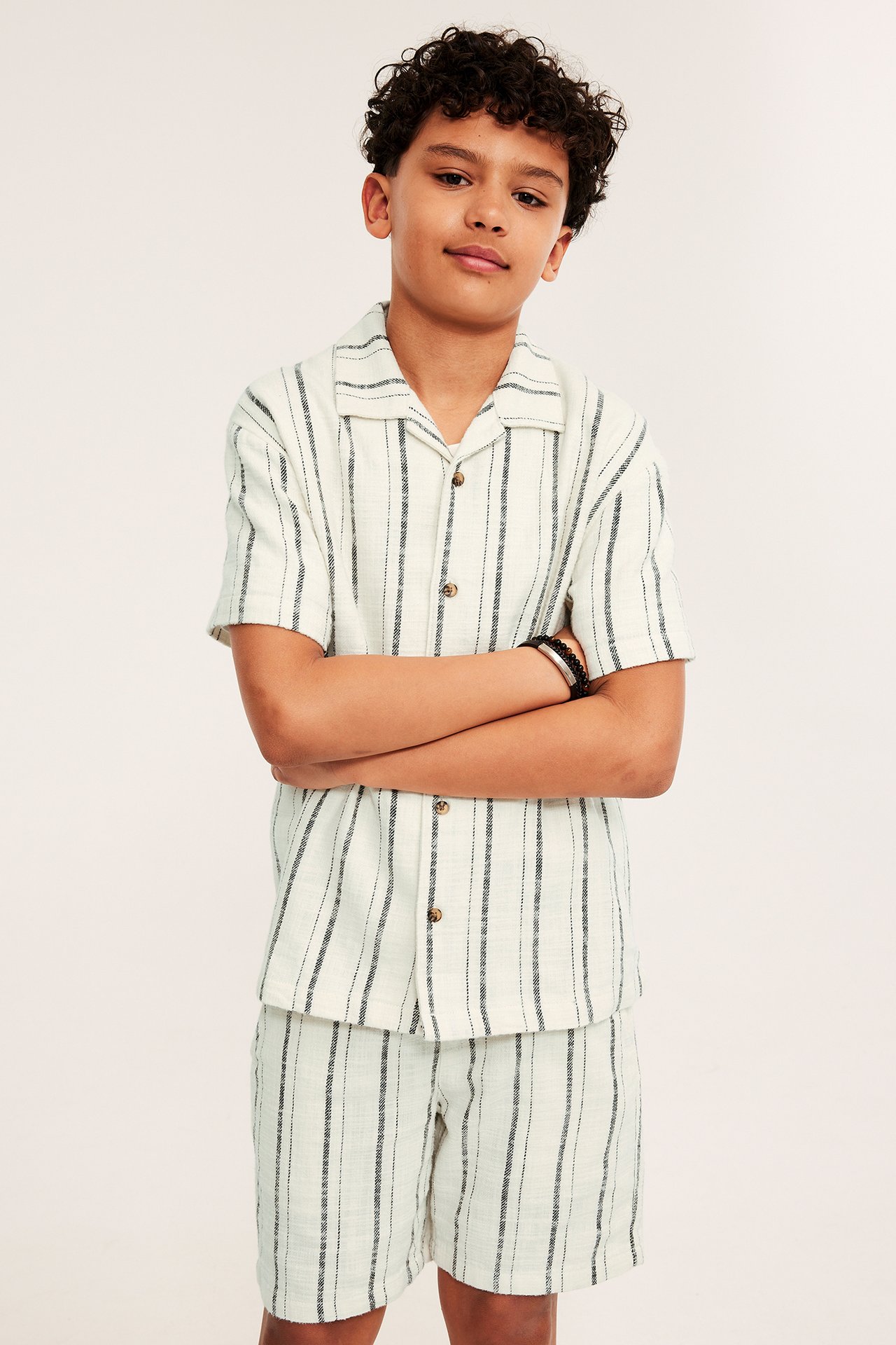 Frontbilde av en gutt i en offwhite stripete bomullsskjorte med resortkrage og matchende shorts.