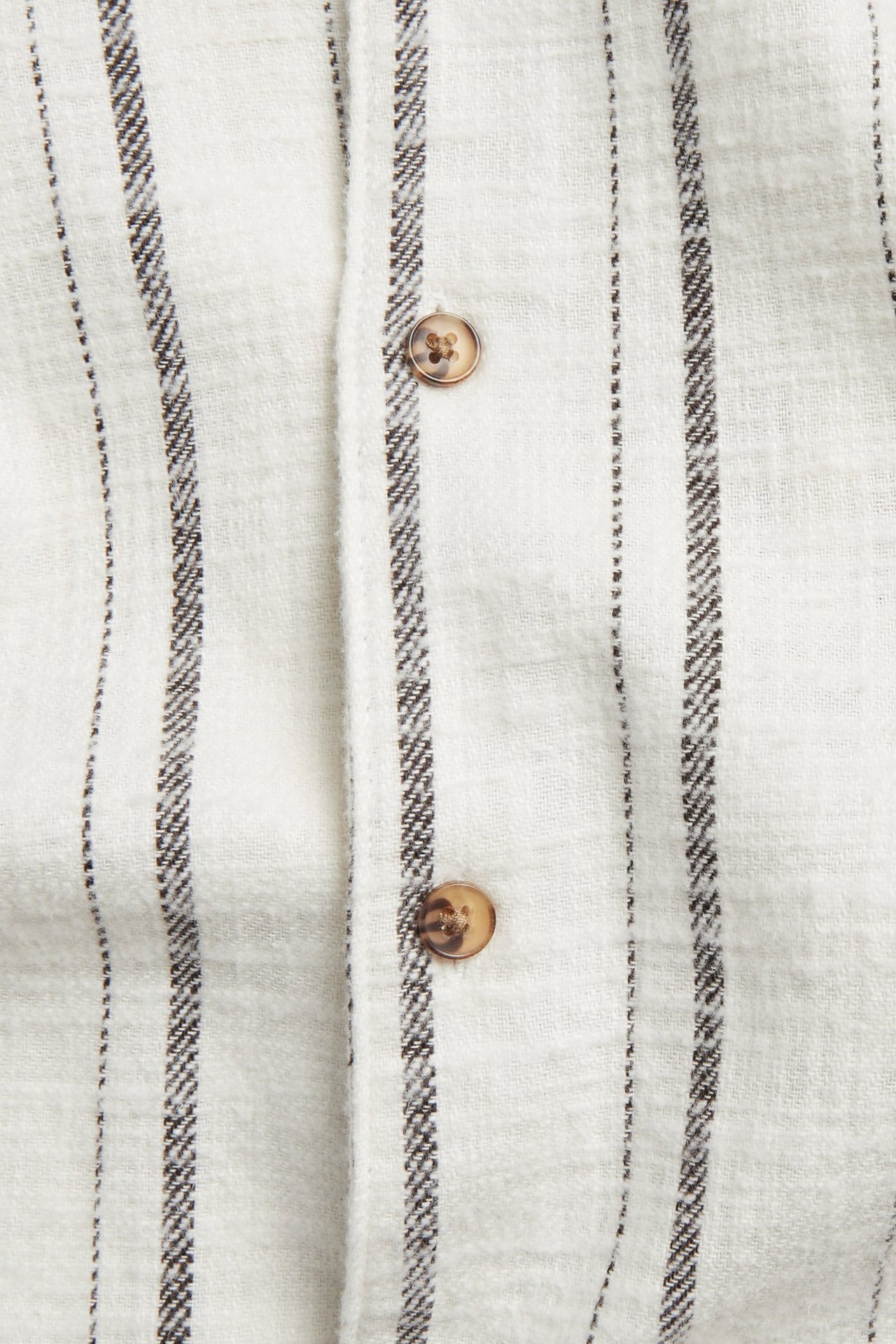 Zbliżenie na białą bawełnianą koszulę w paski o lnianej fakturze i brązowych guzikach.