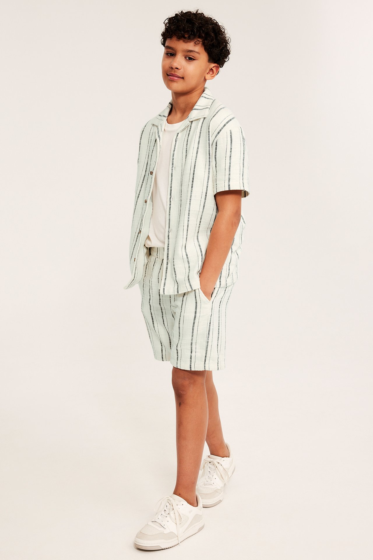 Gutt, frontbilde: Stripete off-white bomullsshorts, matchende åpen skjorte, hvit t-skjorte.
