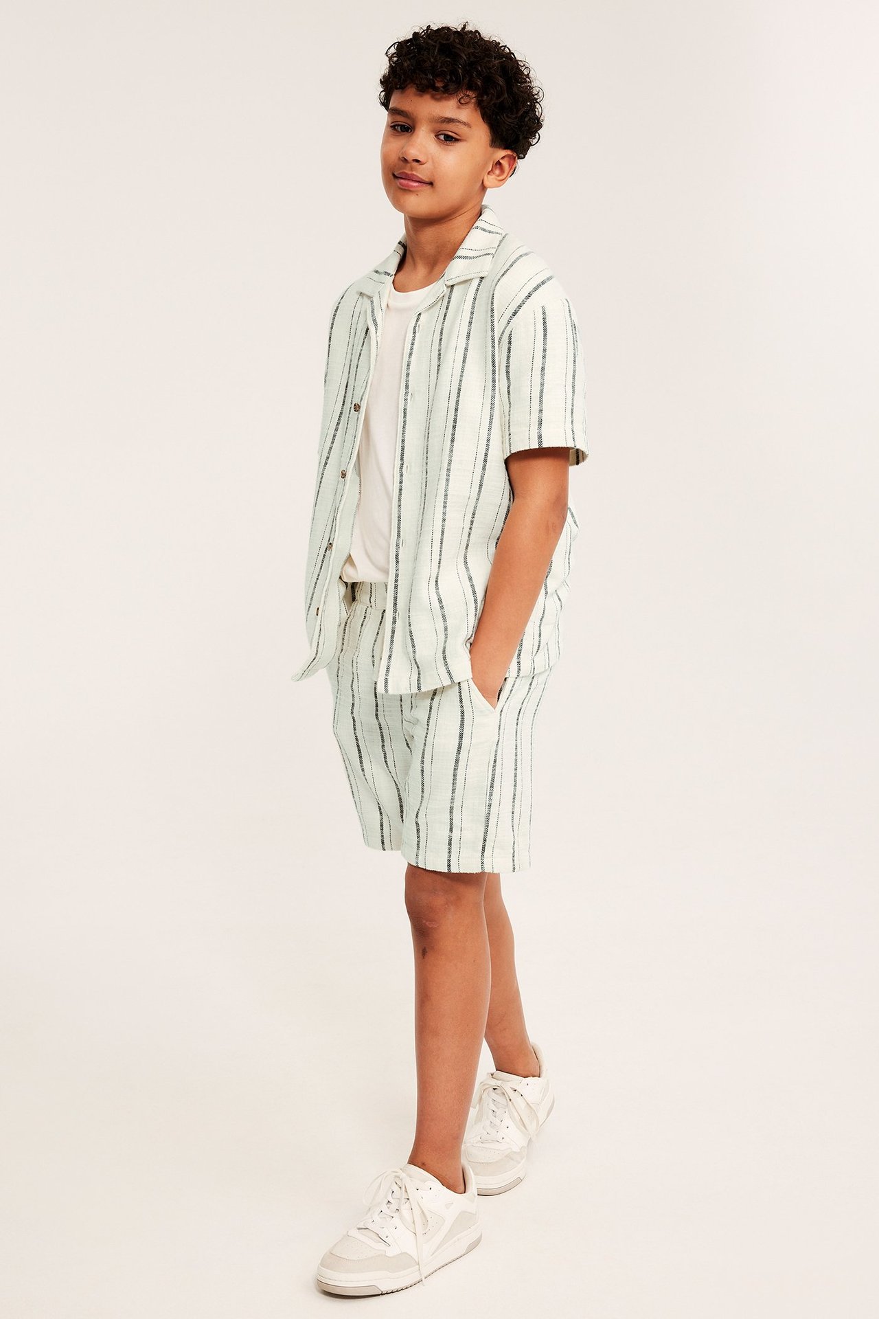 Chłopiec z przodu: Bawełniane szorty w paski ecru, otwarta koszula, biała koszulka.