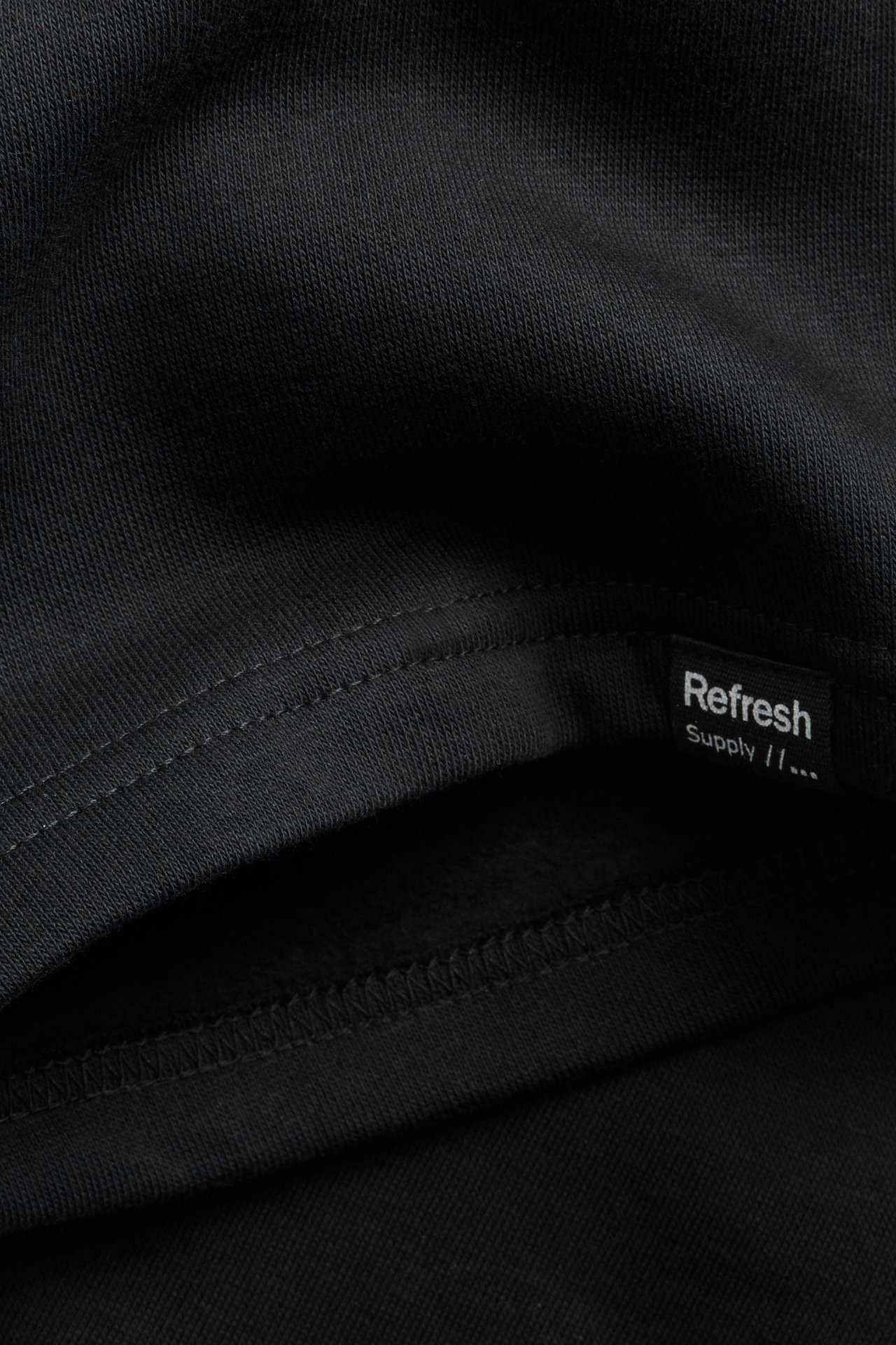 Närbild av svart bomullstrikåtyg för shorts med synlig söm och liten Refresh Supply-etikett.