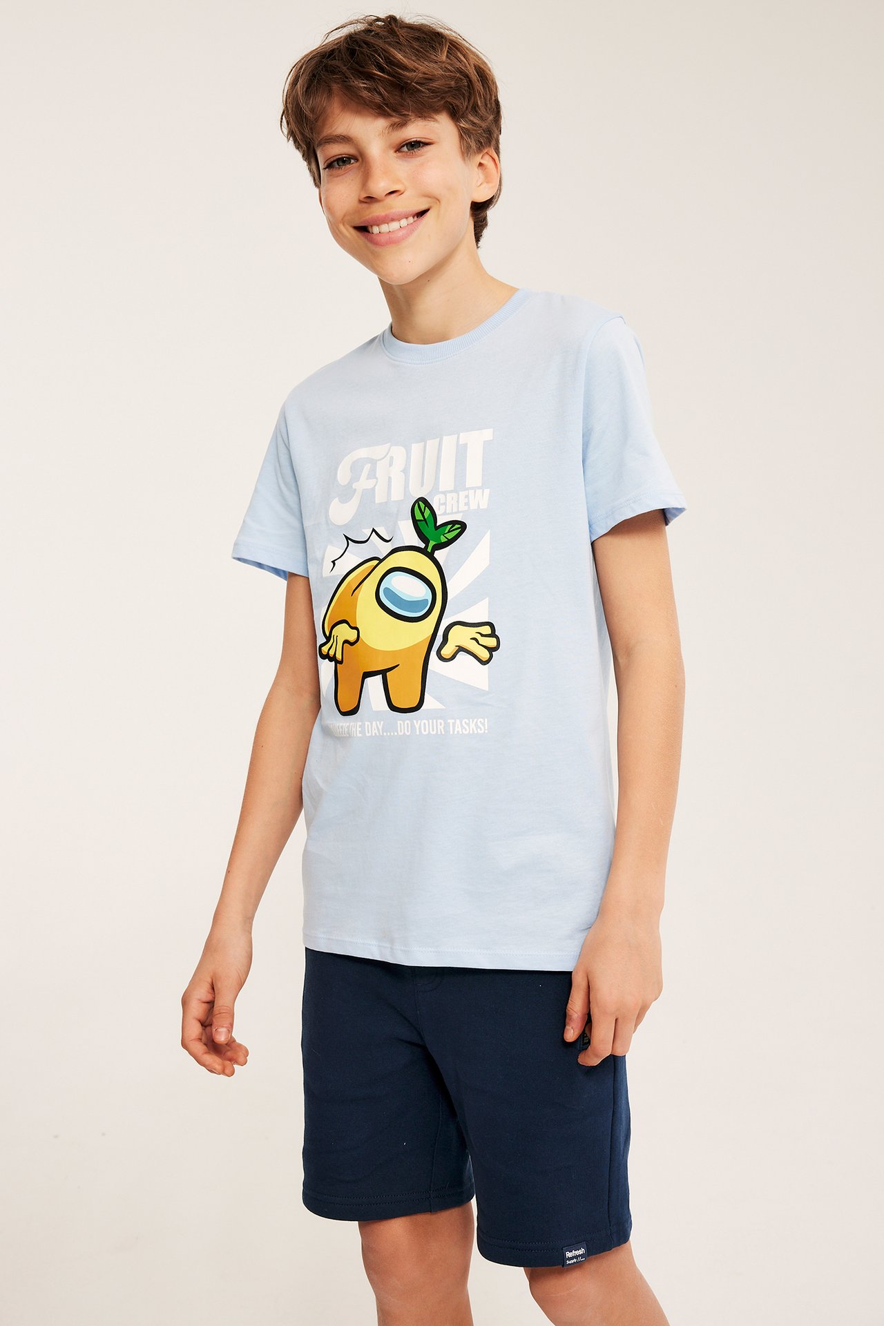 Forfra, et barn i mørkeblå joggeshorts og en lyseblå t-skjorte med grafisk trykk.