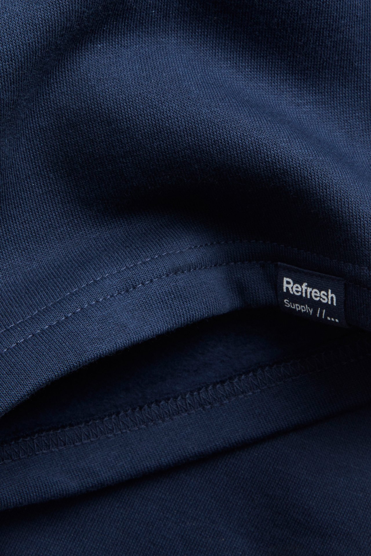 Närbild av mörkblå bomullsjersey sweatshorts, visar sömmar och en liten svart etikett.