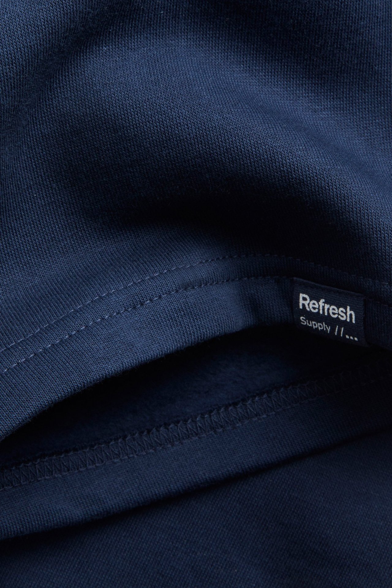 Lähikuva tummansinisestä puuvillaneuloksesta collegeshortseista, jossa tikkaus ja pieni musta etiketti.