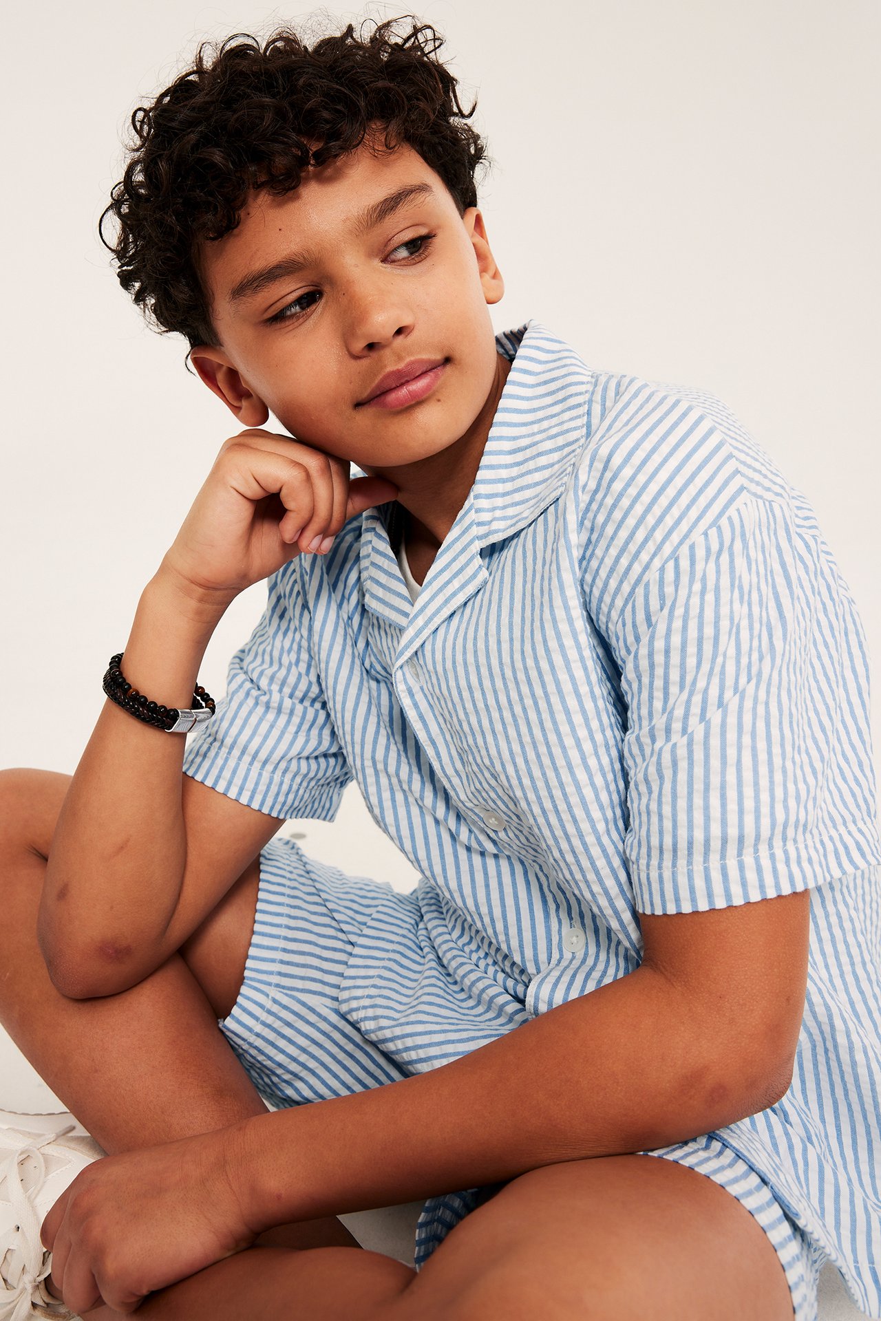 Etunäkymä: Lapsi yllään raidallinen lyhythihainen puuvillapaita, yhteensopivat shortsit ja rannekoru.