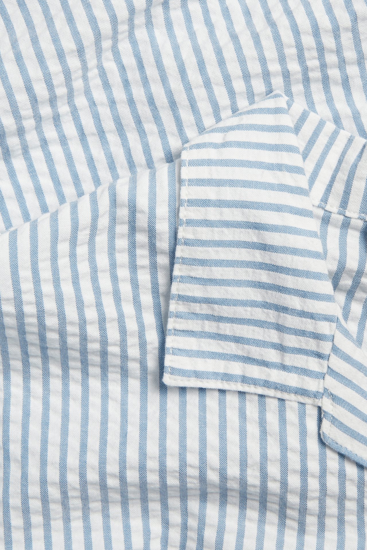 Zbliżenie na niebiesko-białą, pasiastą koszulę z teksturowanej bawełny seersucker.