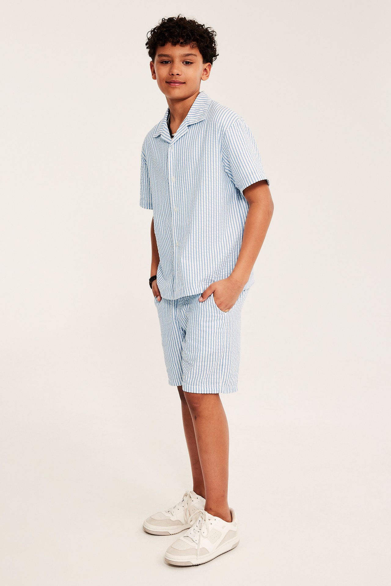 Dziecko w niebiesko-białych pasiastych szortach seersucker i pasującej koszuli z krótkim rękawem, widok z przodu/boku.