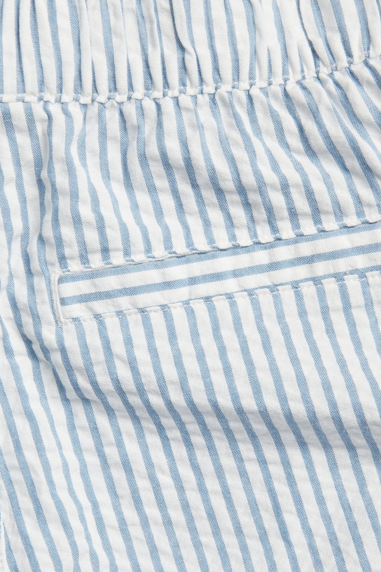 Zbliżenie na niebiesko-białe szorty z seersuckera w paski, z elastyczną talią i małą kieszenią.