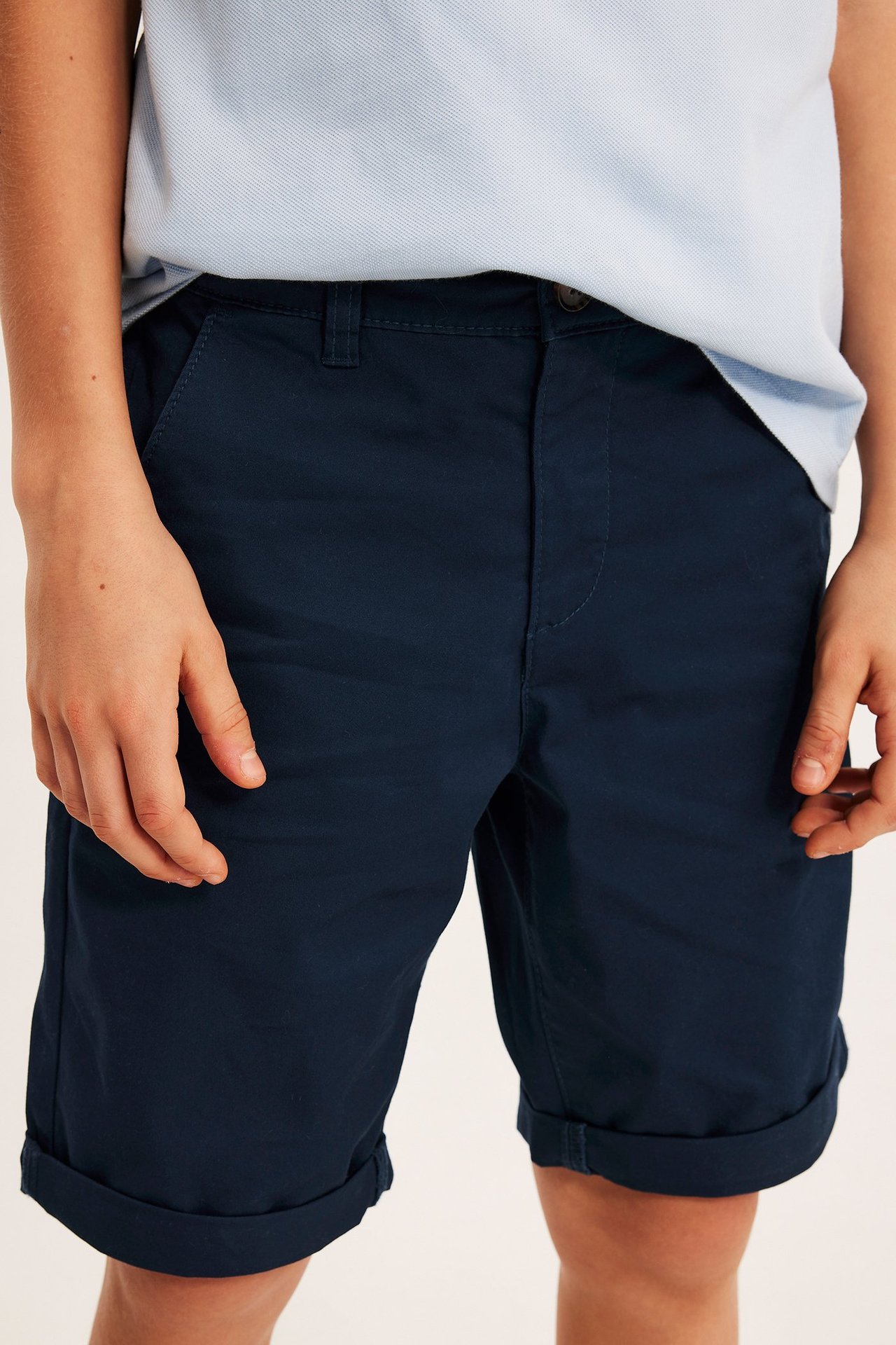 Etukuva lapsesta yllään tummansiniset puuvillatwillishortsit käännetyin lahkein ja vaaleansininen pikeepaita.