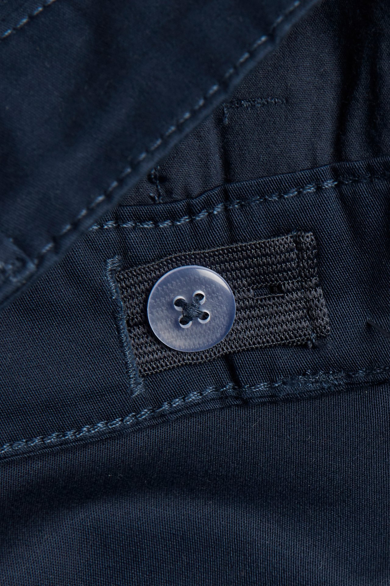 Zbliżenie na granatowe dziecięce szorty chino z twillu bawełnianego z regulowanym guzikiem w pasie.