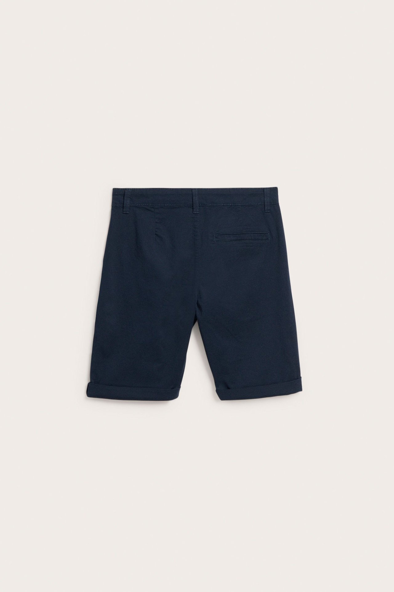 Widok z tyłu: ciemnoniebieskie dziecięce szorty chino z bawełnianego twillu z podwiniętymi nogawkami i tylnymi kieszeniami.