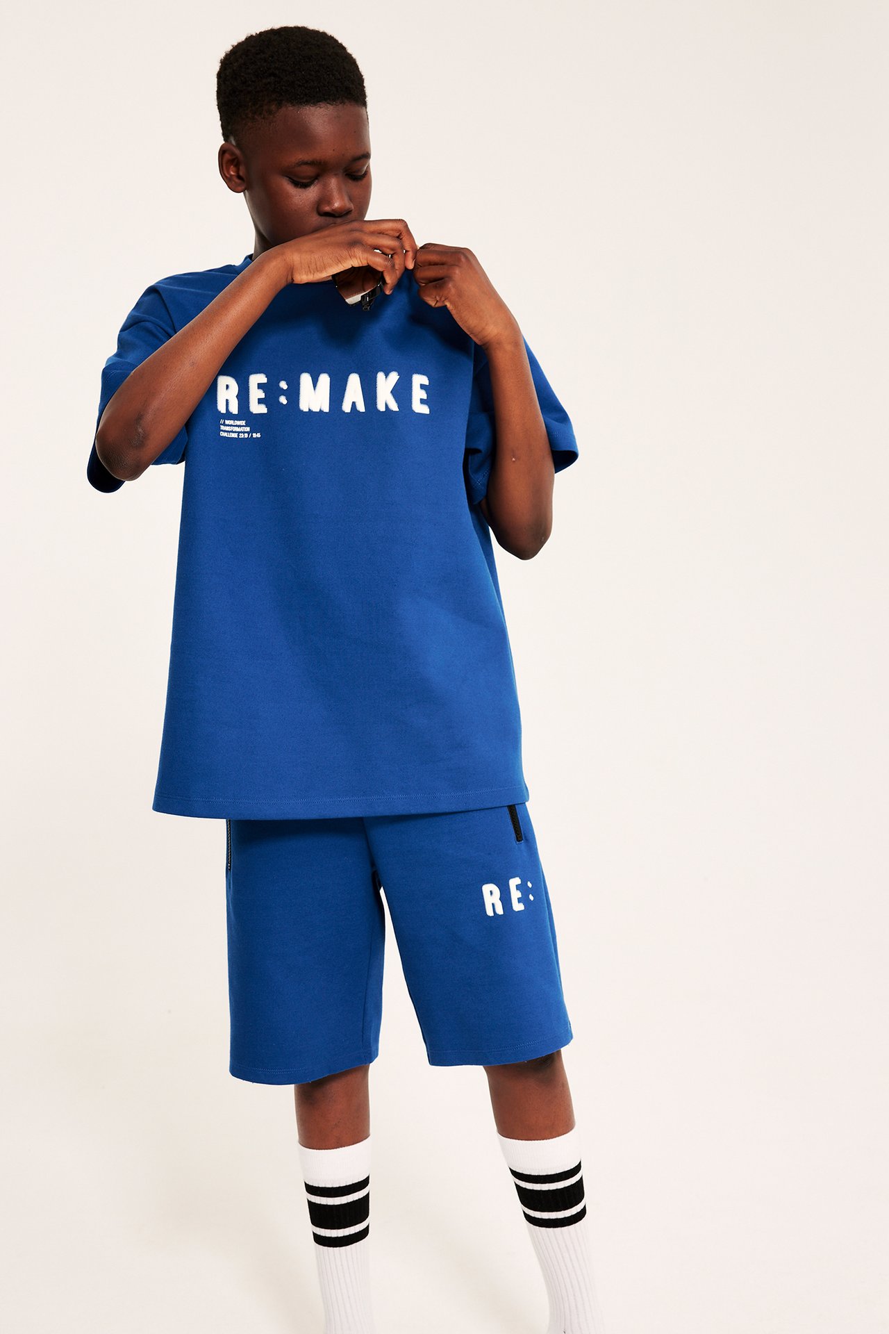 Frontvy av barn i mörkblå interlockshorts med texttryck, dragkedjor, matchande t-shirt och randiga strumpor.
