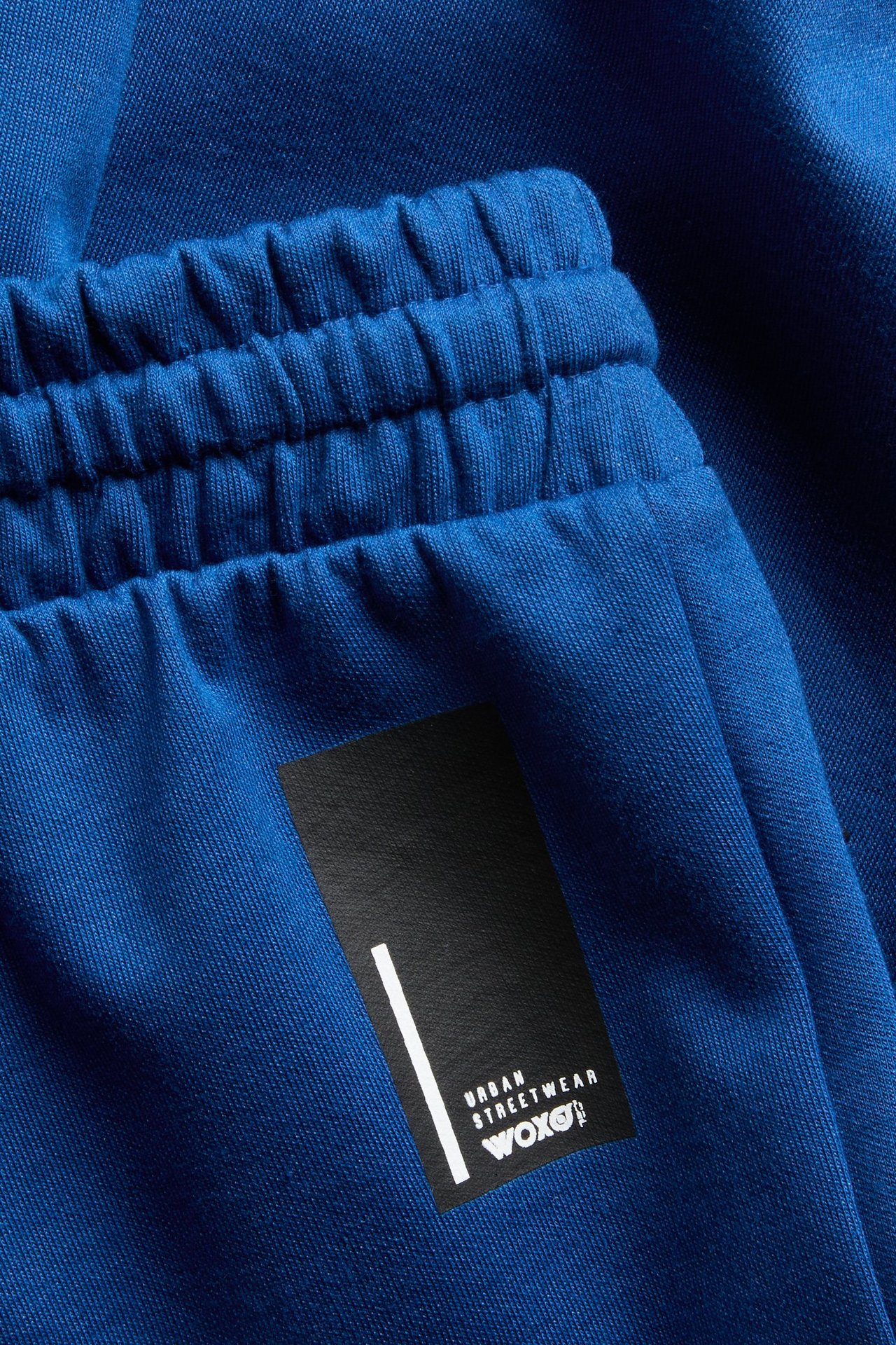 Närbild på mörkblå sportiga barnshorts med resårlinning och svart "URBAN STREETWEAR WOXO!" textprint.