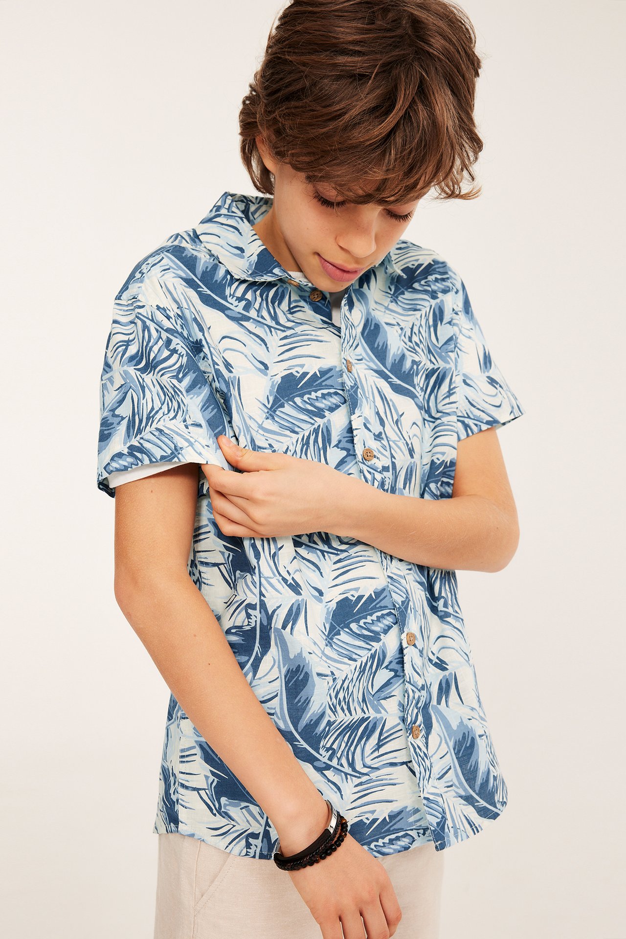 Etunäkymä: Lapsi yllään luonnonvalkoinen ja sinikuvioinen lyhythihainen puuvillapaita napeilla ja mustalla rannekorulla.