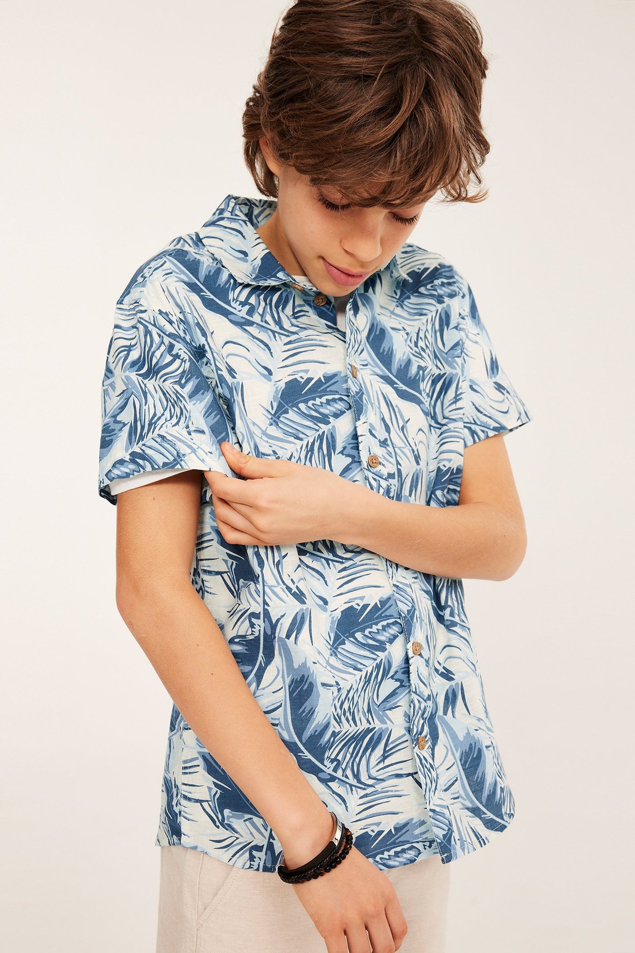 Frontvy: Kid i en benvit och blåmönstrad kortärmad bomullsskjorta med knappar och ett svart armband.