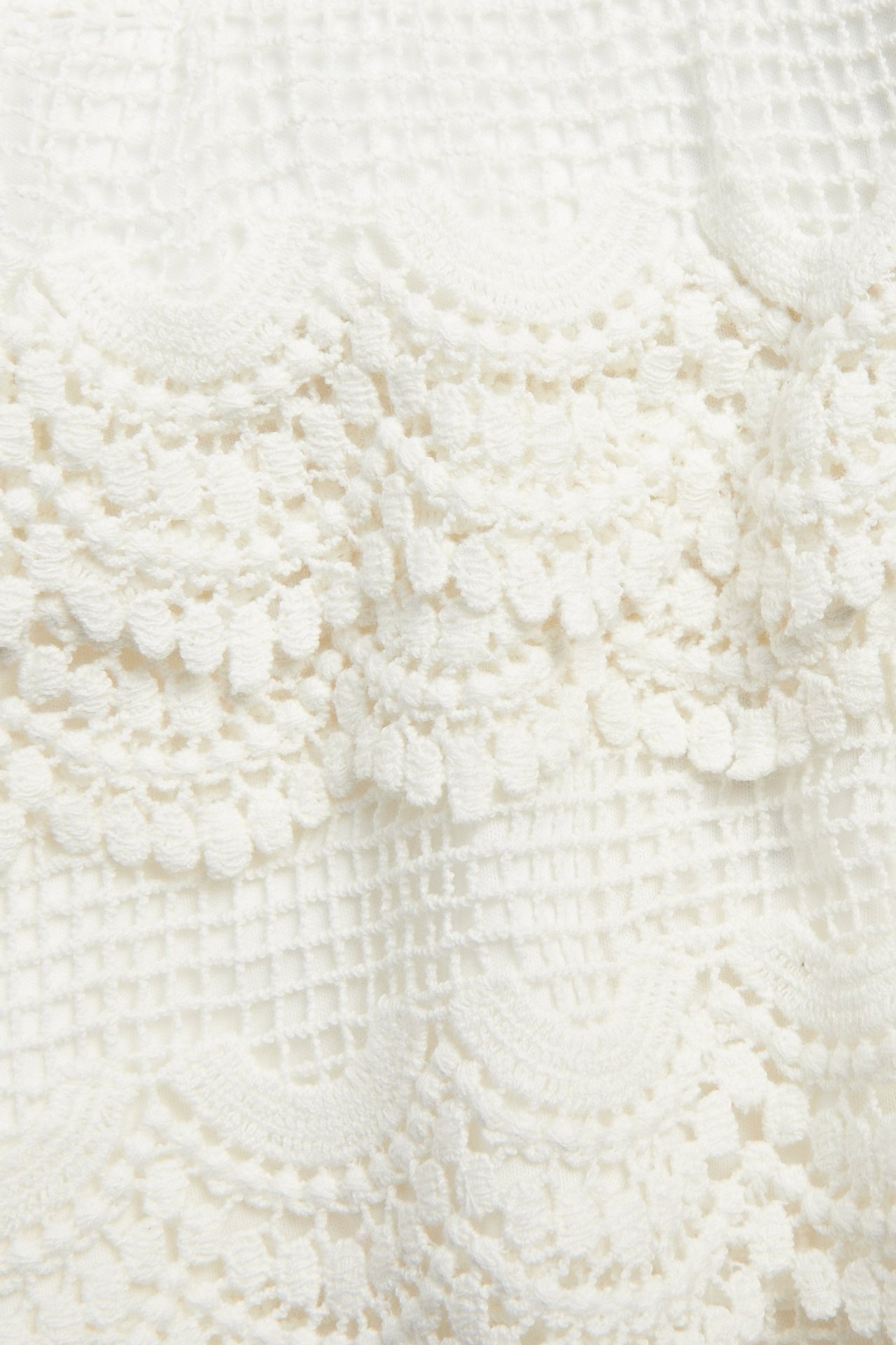 Zbliżenie off-white koronkowych szortów z różnorodnymi wzorami i falowanymi krawędziami.