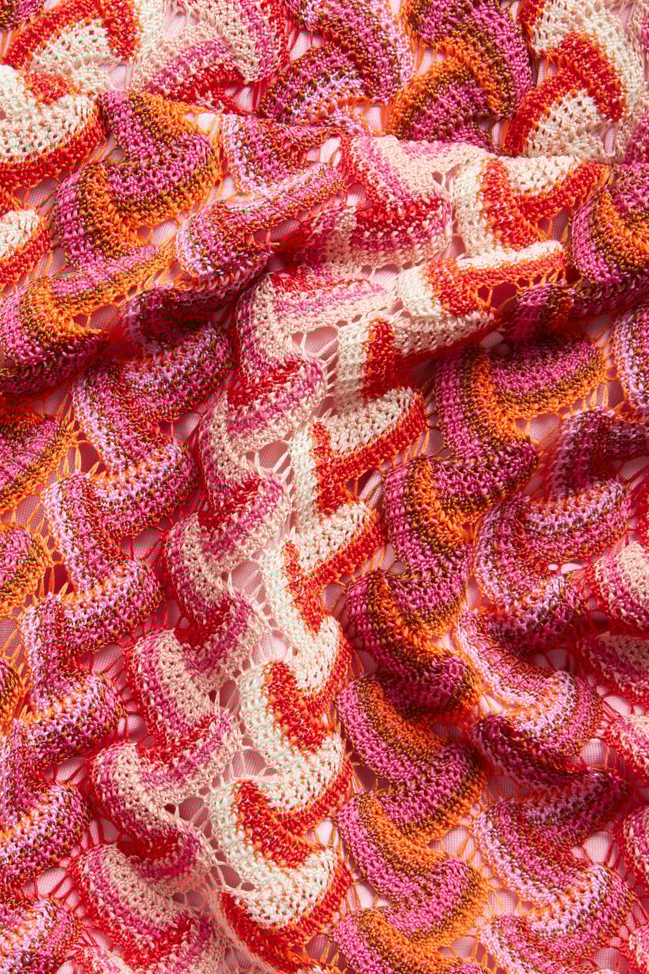 Zbliżenie na różowy, pomarańczowy, czerwony i kremowy szydełkowy dżersej z falistym wzorem na szorty.