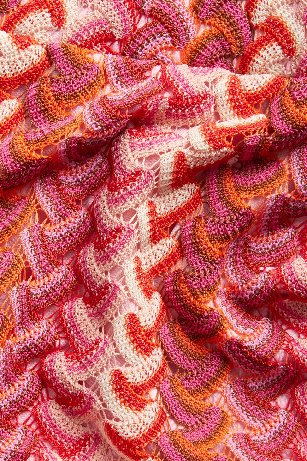 Zbliżenie na różowy, pomarańczowy, czerwony i kremowy szydełkowy dżersej z falistym wzorem na szorty.