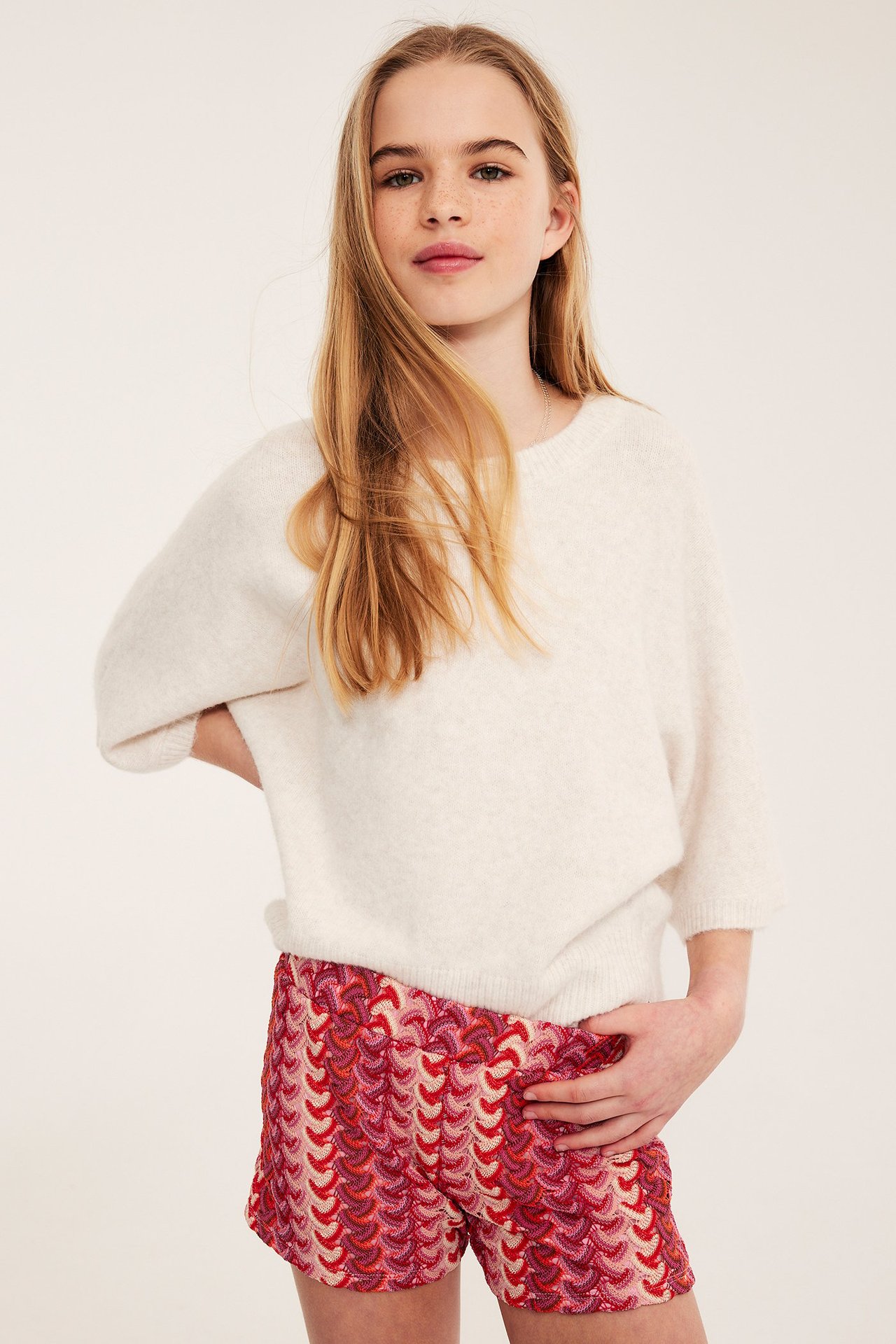Dziewczynka w białym swetrze i różowych shortsach z koronką.