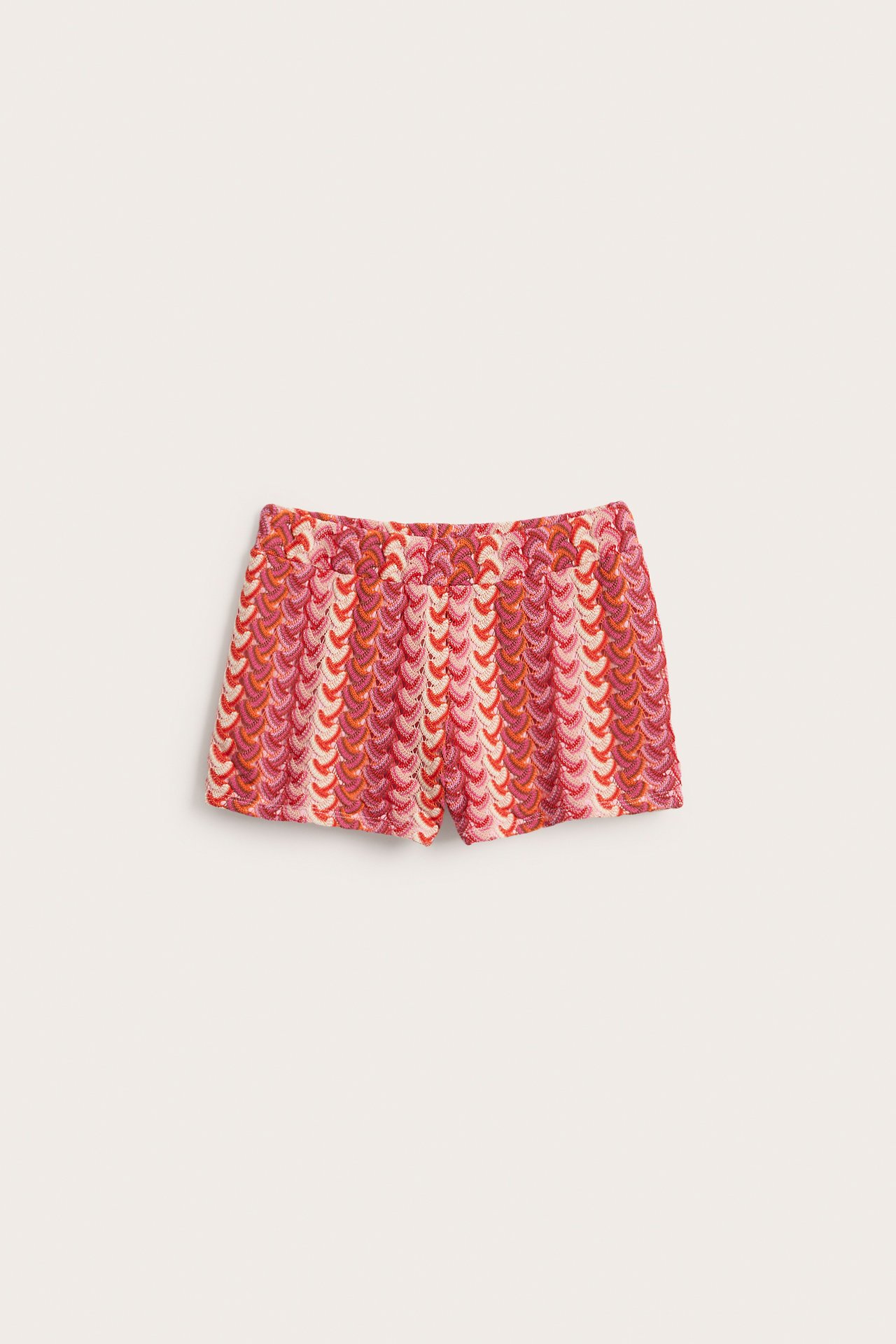 Widok z przodu różowo-czerwonych krótkich szortów z szydełkowanym wzorem i gumką w pasie.