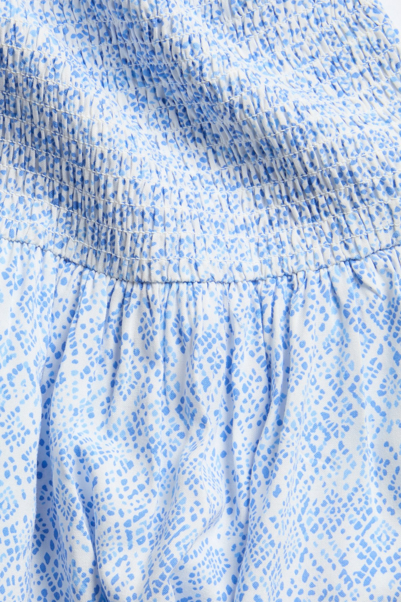 Zbliżenie białej sukienki z niebieskim wzorzystym detalem marszczenia.
