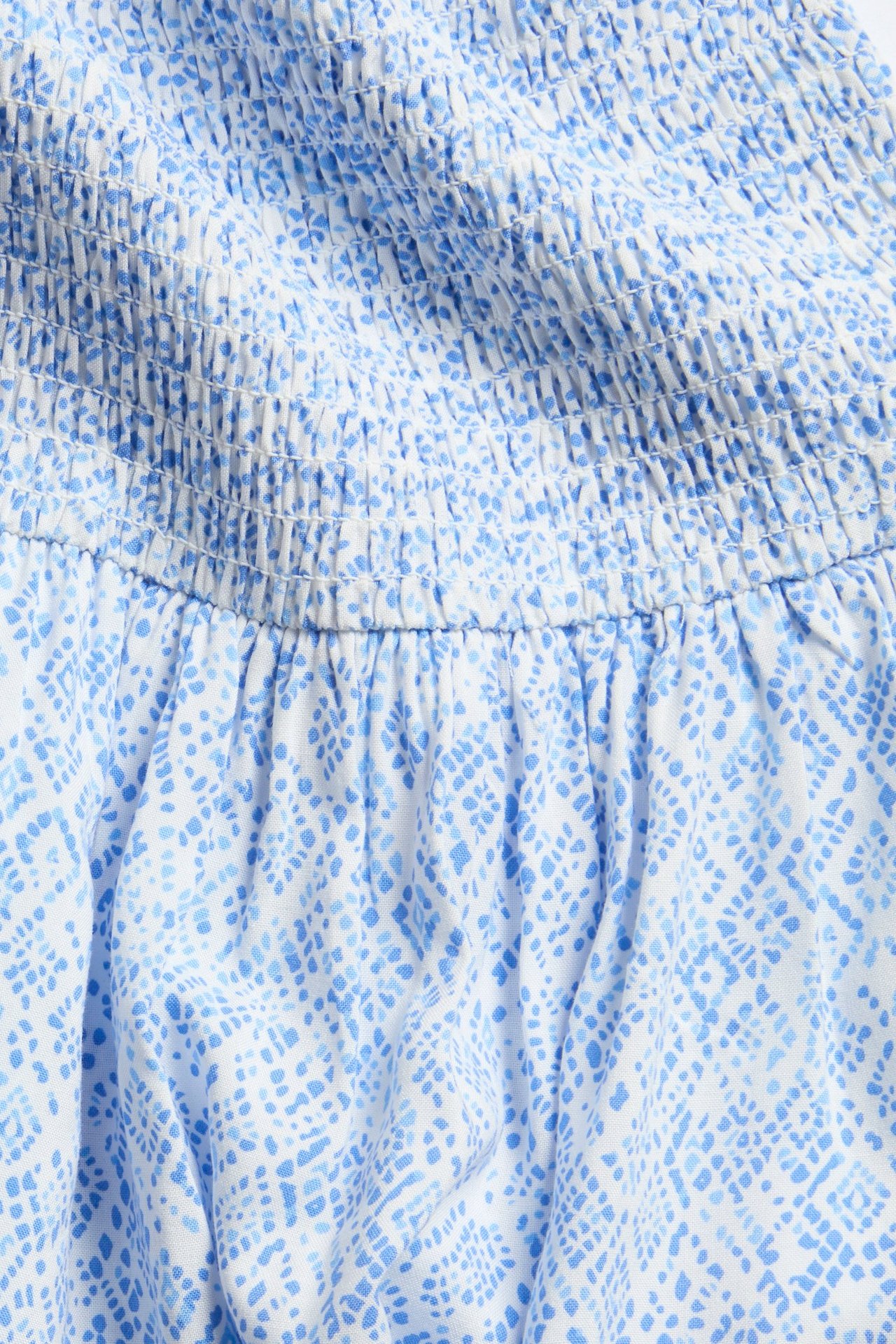 Zbliżenie białej sukienki z niebieskim wzorzystym detalem marszczenia.