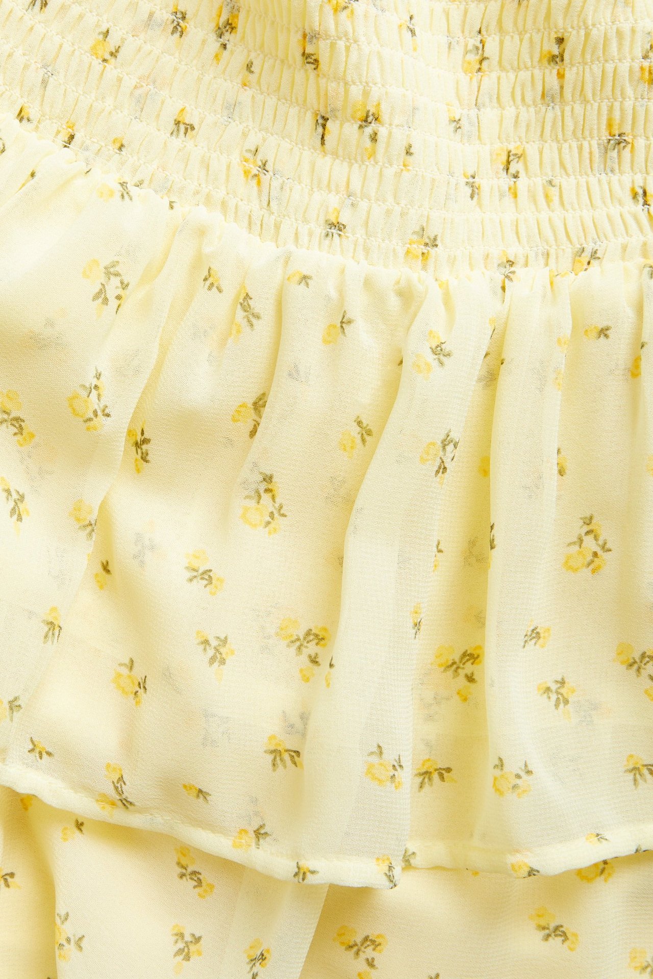 Närbild på en ljusgul mönstrad volangkjol för barn, med smock och litet gult blommönster.