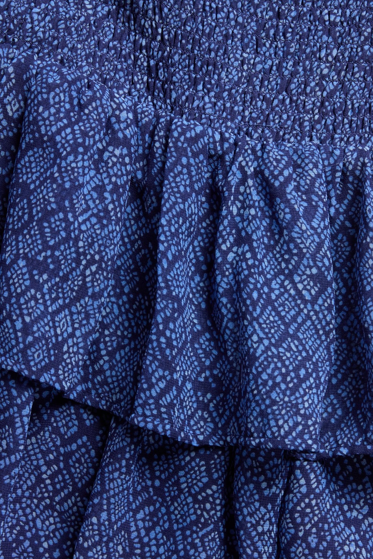 Zbliżenie na ciemnoniebieską, wzorzystą spódnicę poliestrową z falbanami i marszczonym pasem.