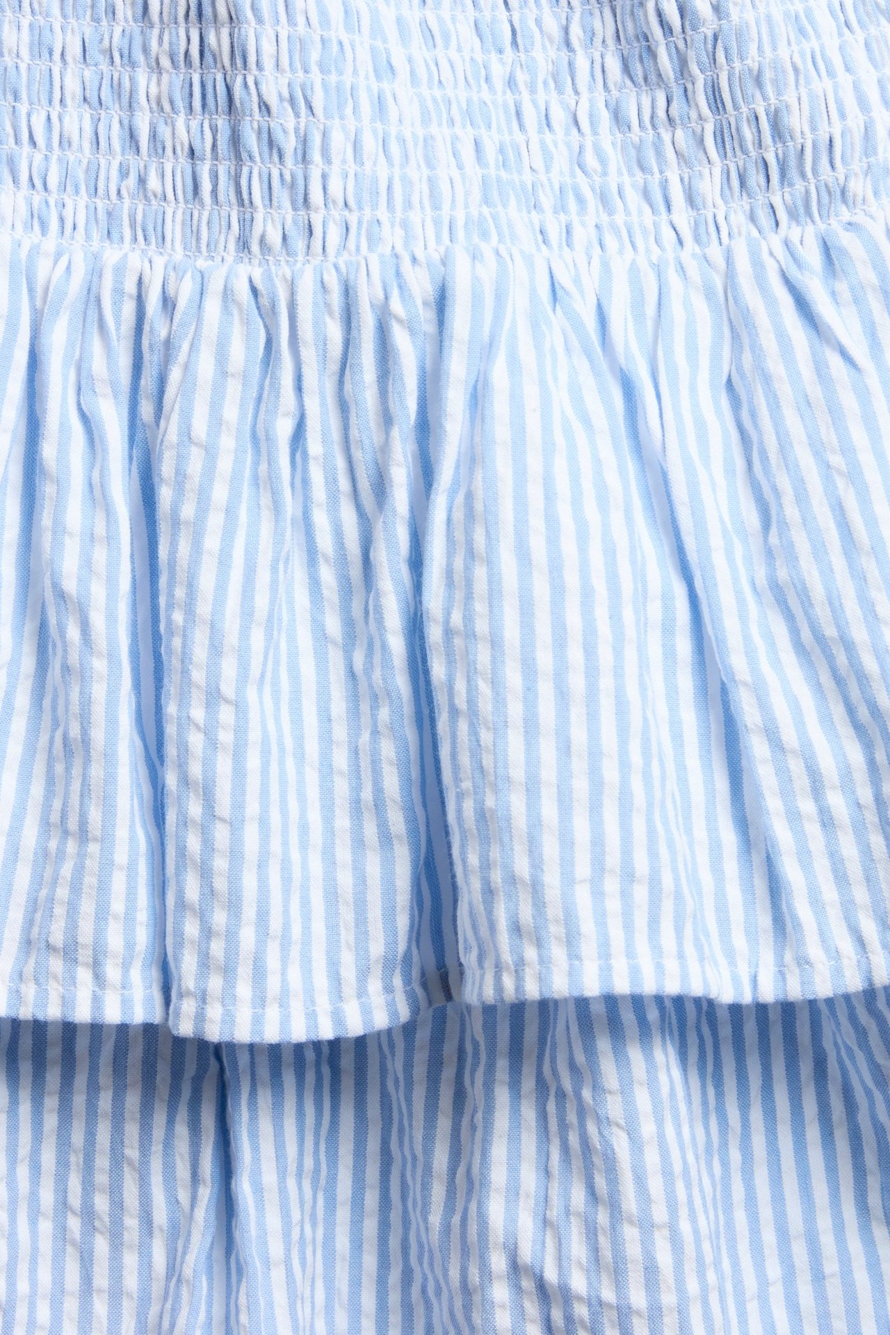 Närbild av en ljusblå- och vitrandig volangkjol med rynkad midja.