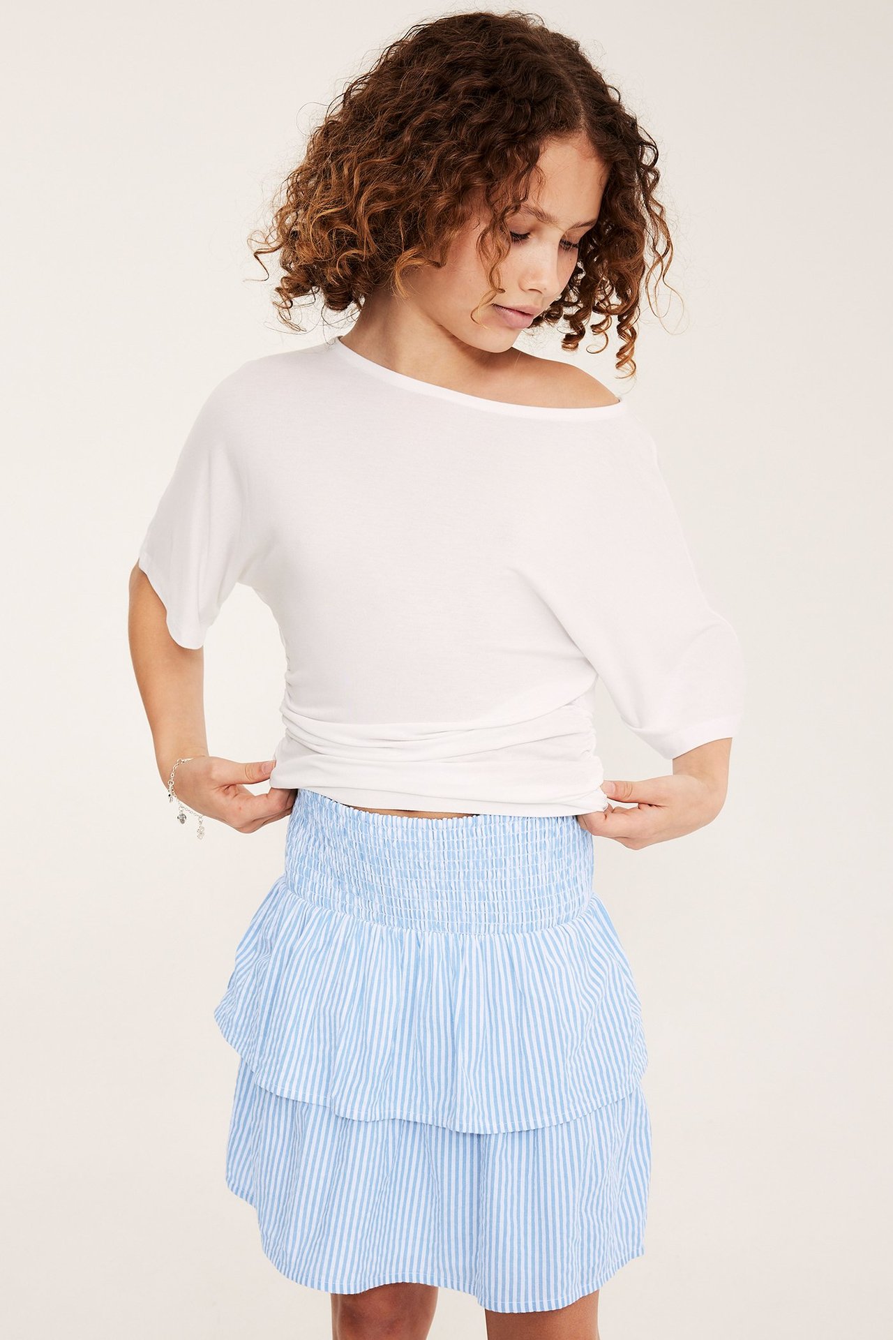 Framifrån: Barn i ljusblå och vitrandig volangkjol, vit topp och silverarmband.