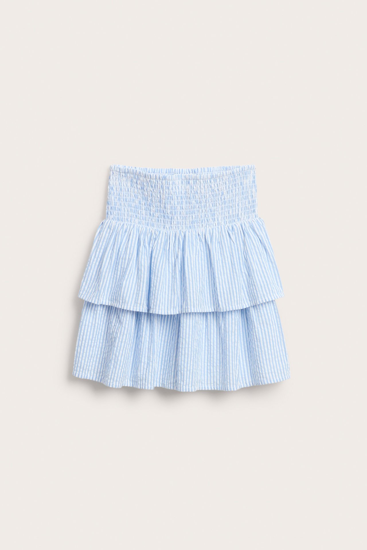 Framifrån, en randig volangkjol för barn i ljusblått och vitt med smockad midja.