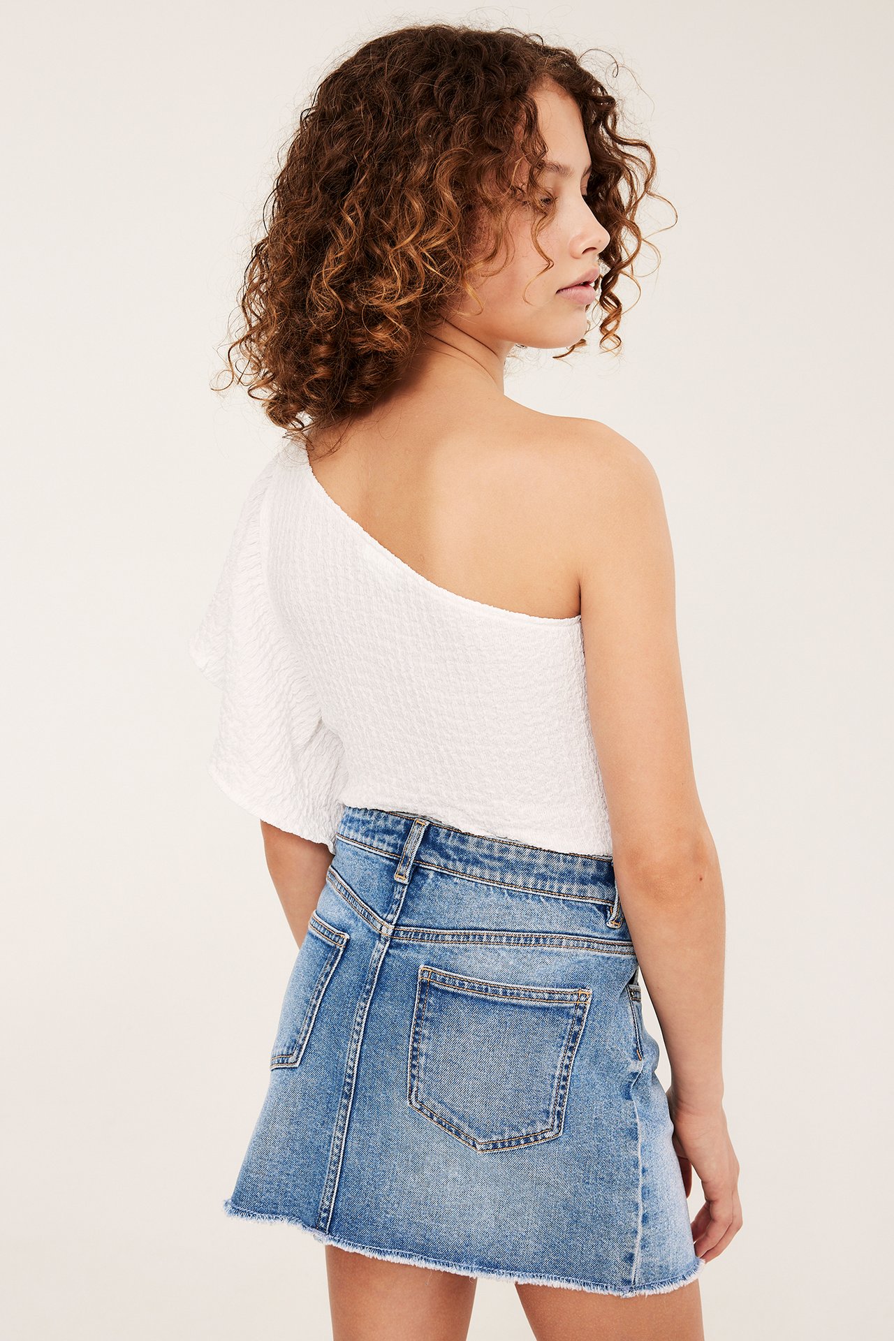 Barns ryggutsikt i lyseblått lavt liv dongeriskjørt med frynsete kant og hvit en-skulder topp.