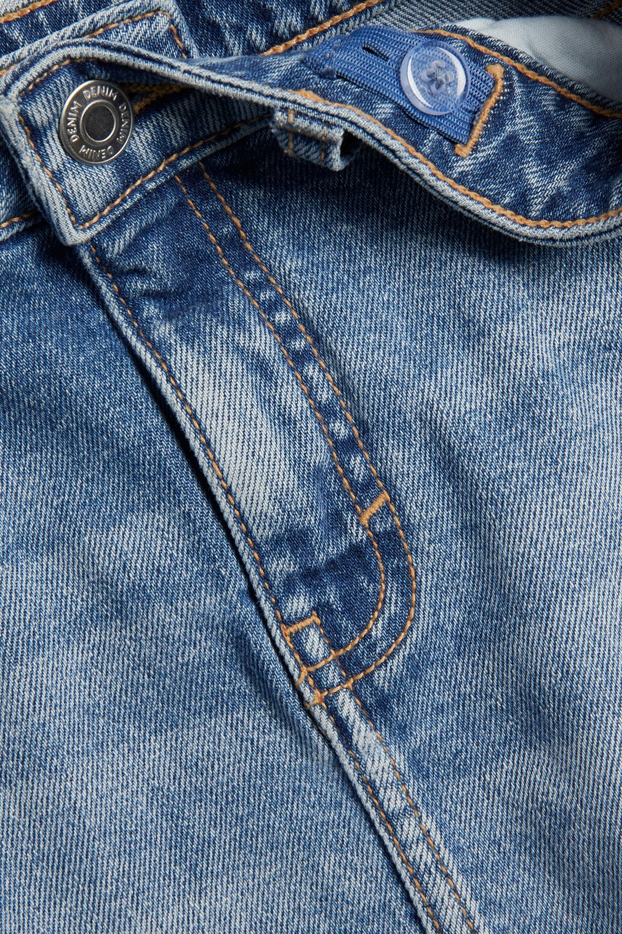 Närbild av ljusblå jeanskjol med låg midja, metallknapp och justerbar resår inuti.