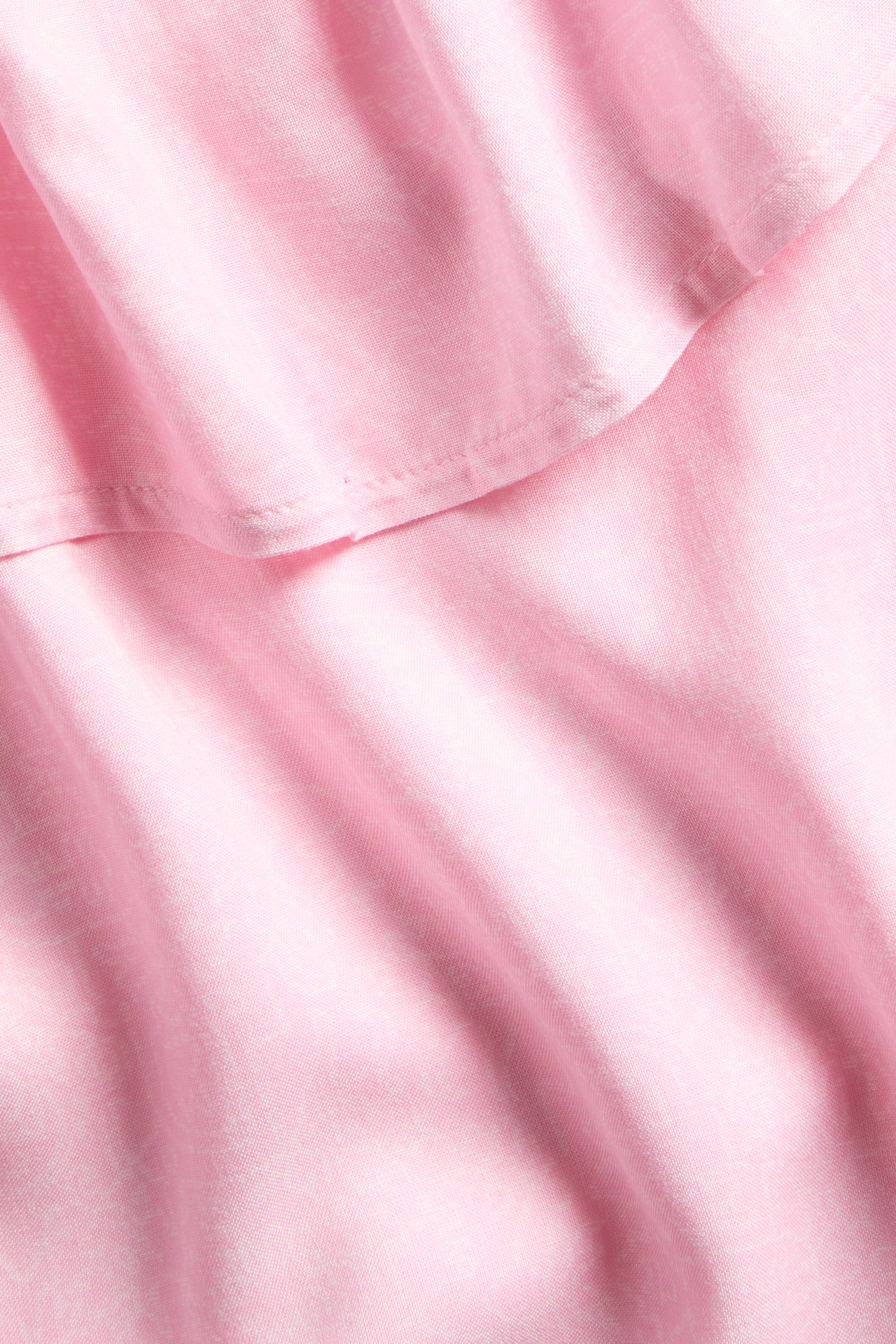 Lähikuva vaaleanpunaisesta viskoosimekon kankaasta, jossa on pehmeä röyhelö.