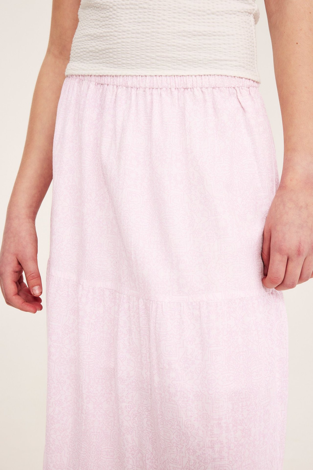 Lähikuva: Lapsi vaaleanpunaisessa kuviollisessa maksihameessa, joustovyötäröllä, ja valkoisessa topissa.