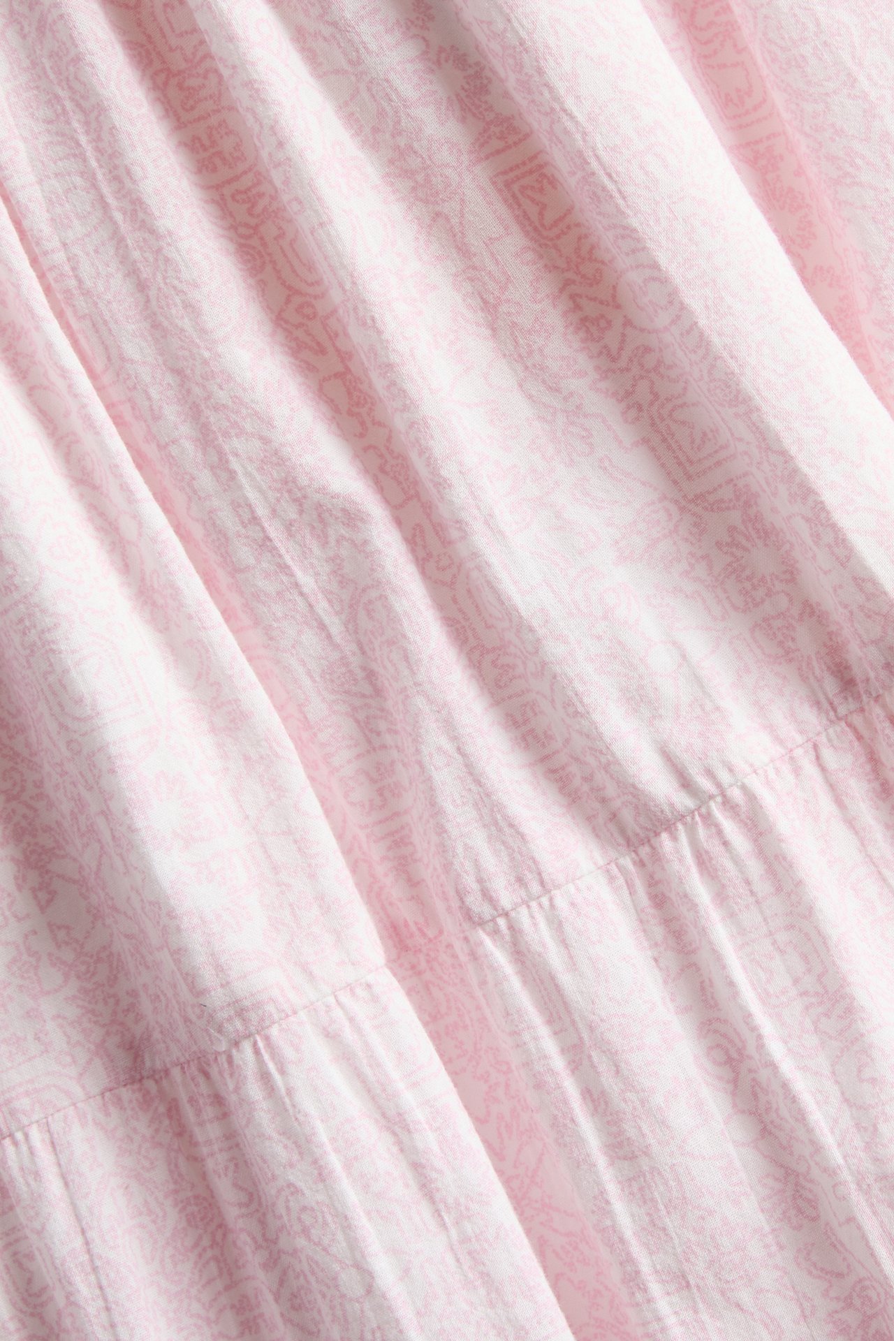 Lähikuva vaaleanpunaisesta kuviollisesta puuvillaisesta maksihameesta, jossa on abstrakti kuvio ja kerroksellinen muotoilu.