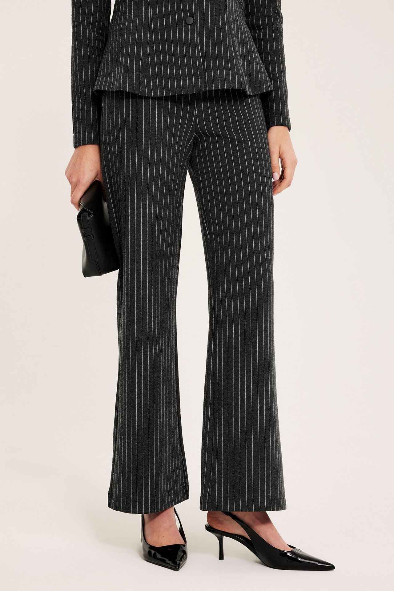 Kvinne, forfra: mørkegrå nålestripete vide bukser, matchende blazer, svart clutch og svarte hæler.