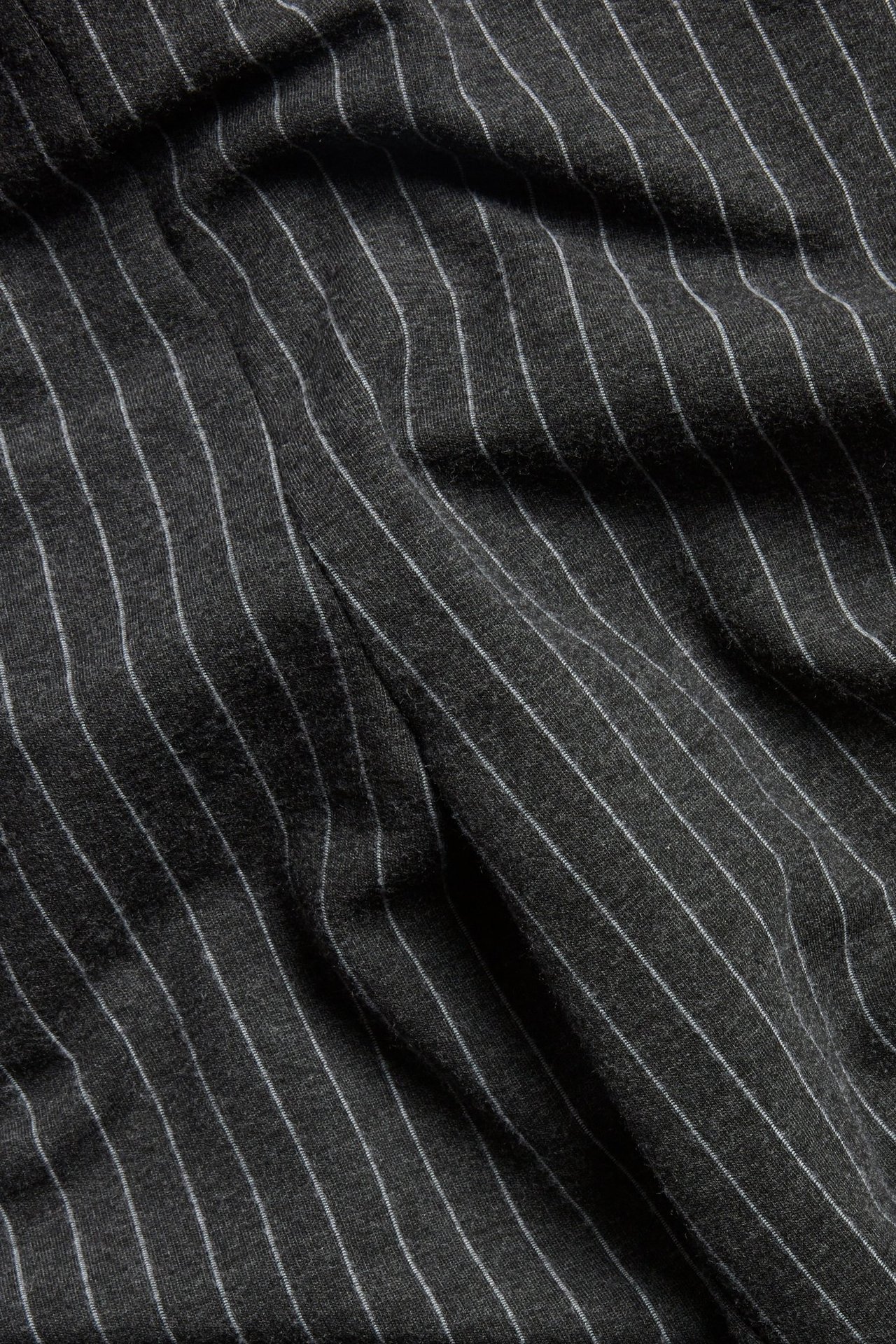 Zbliżenie ciemnoszarego melanżowego materiału spodni w prążki z widocznymi białymi paskami.