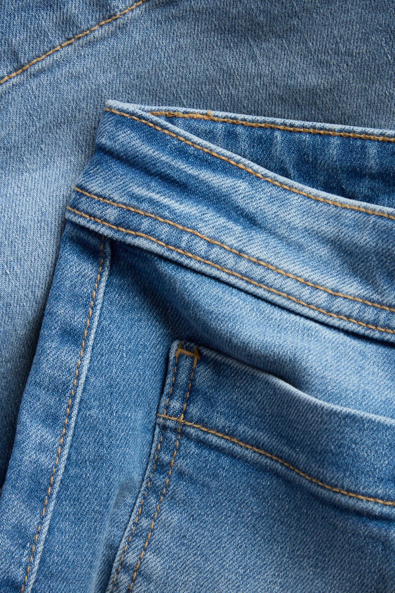 Nærbilde av lyseblå denimshorts med synlige oransje sømmer og lappelommer.