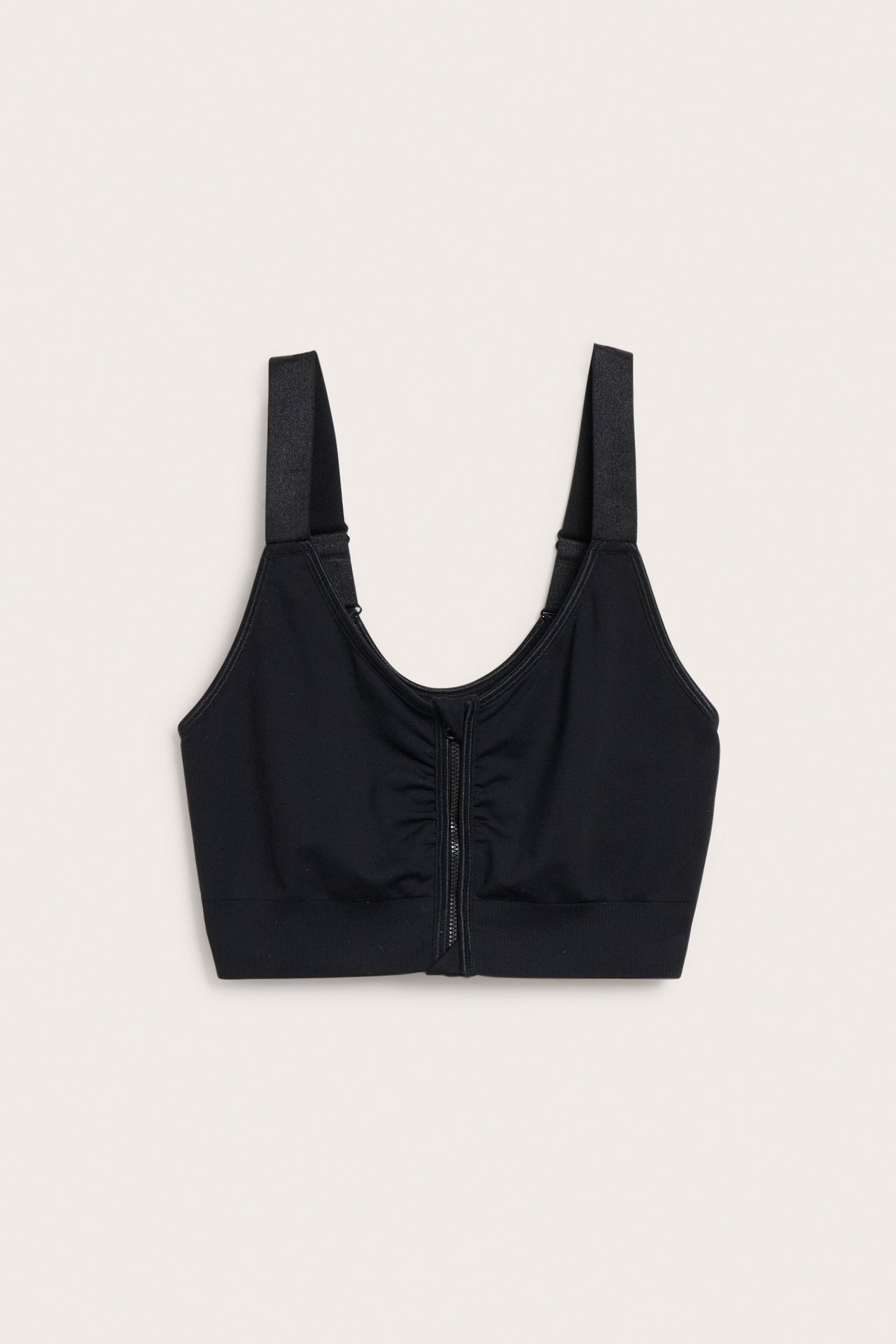 Frontvisning av en svart sømløs BH med brede stropper og glidelås med hektelås foran.