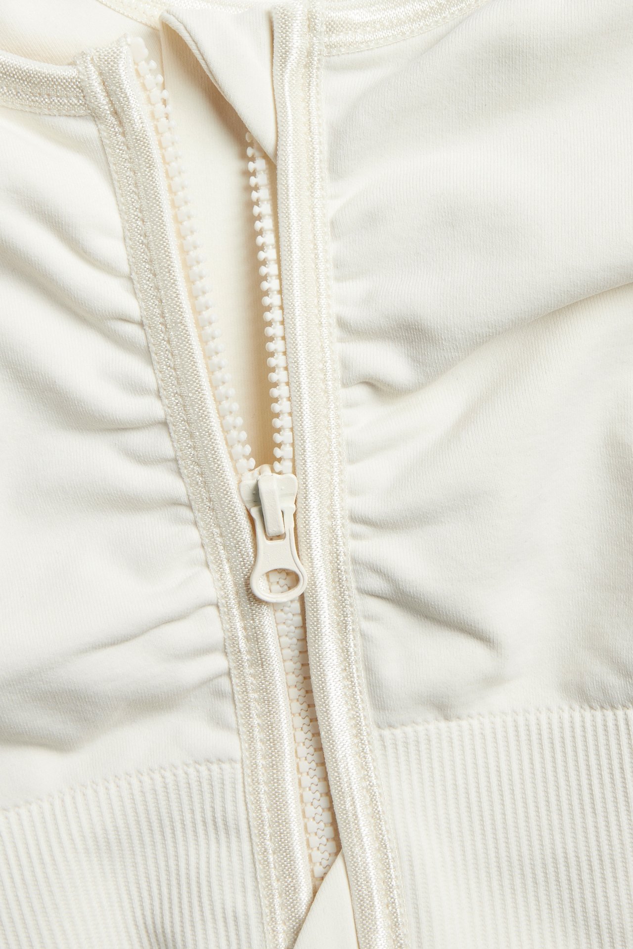 Nærbilde av en offwhite sømløs BH med glidelås foran og ribbedetaljer på det elastiske stoffet.