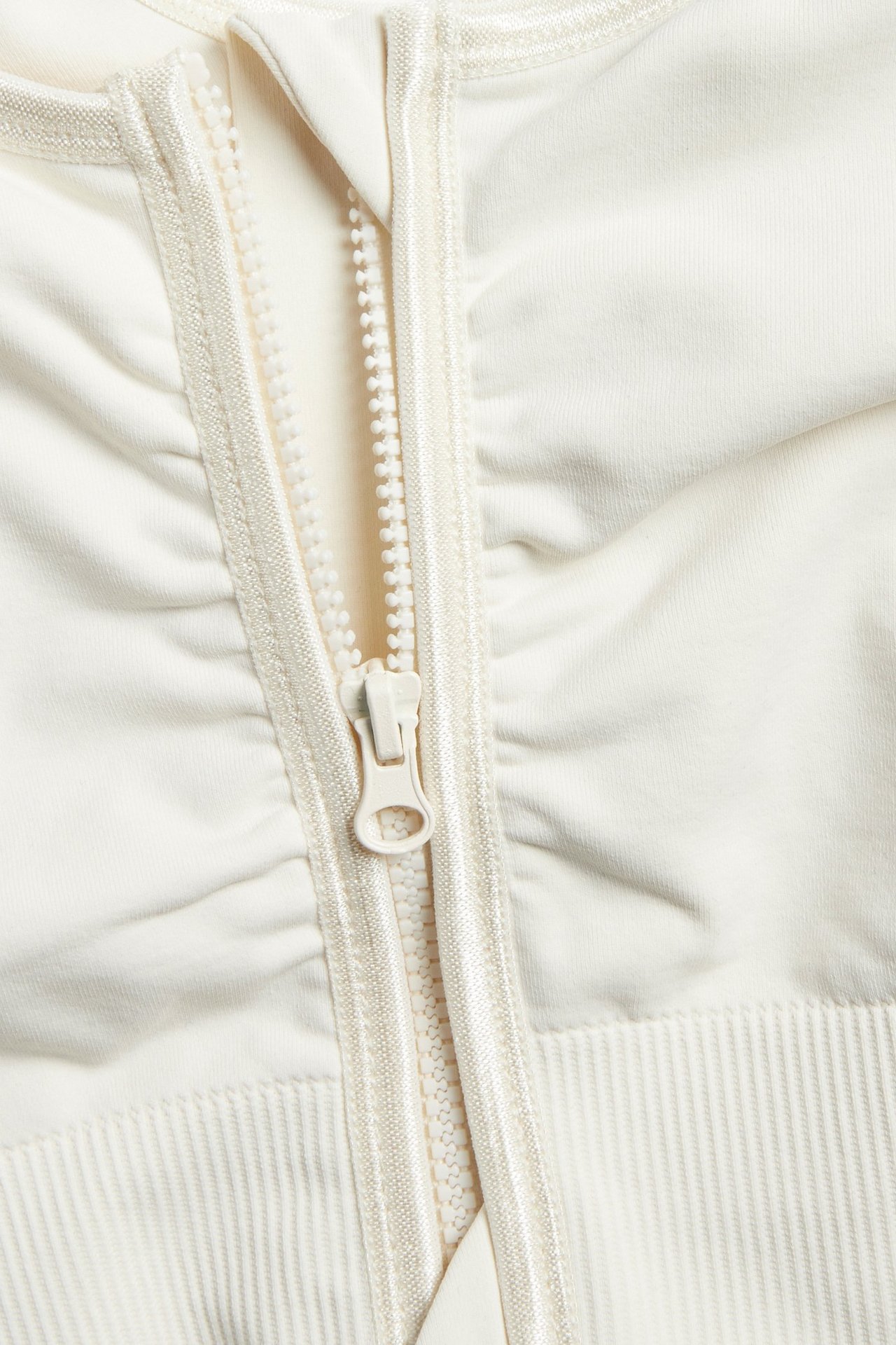 Nærbilde av en offwhite sømløs BH med glidelås foran og ribbedetaljer på det elastiske stoffet.