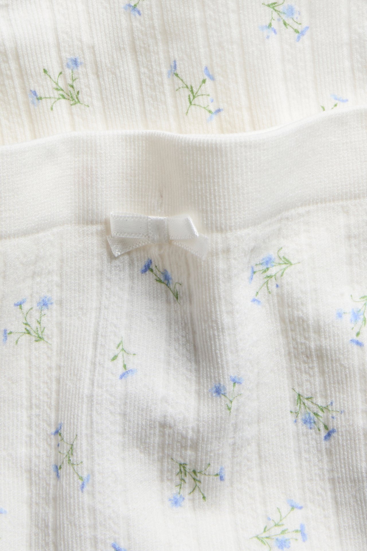 Nærbilde av hvite sømløse hipster-truser med ribbet tekstur, blått blomstermønster og en liten hvit sløyfe.