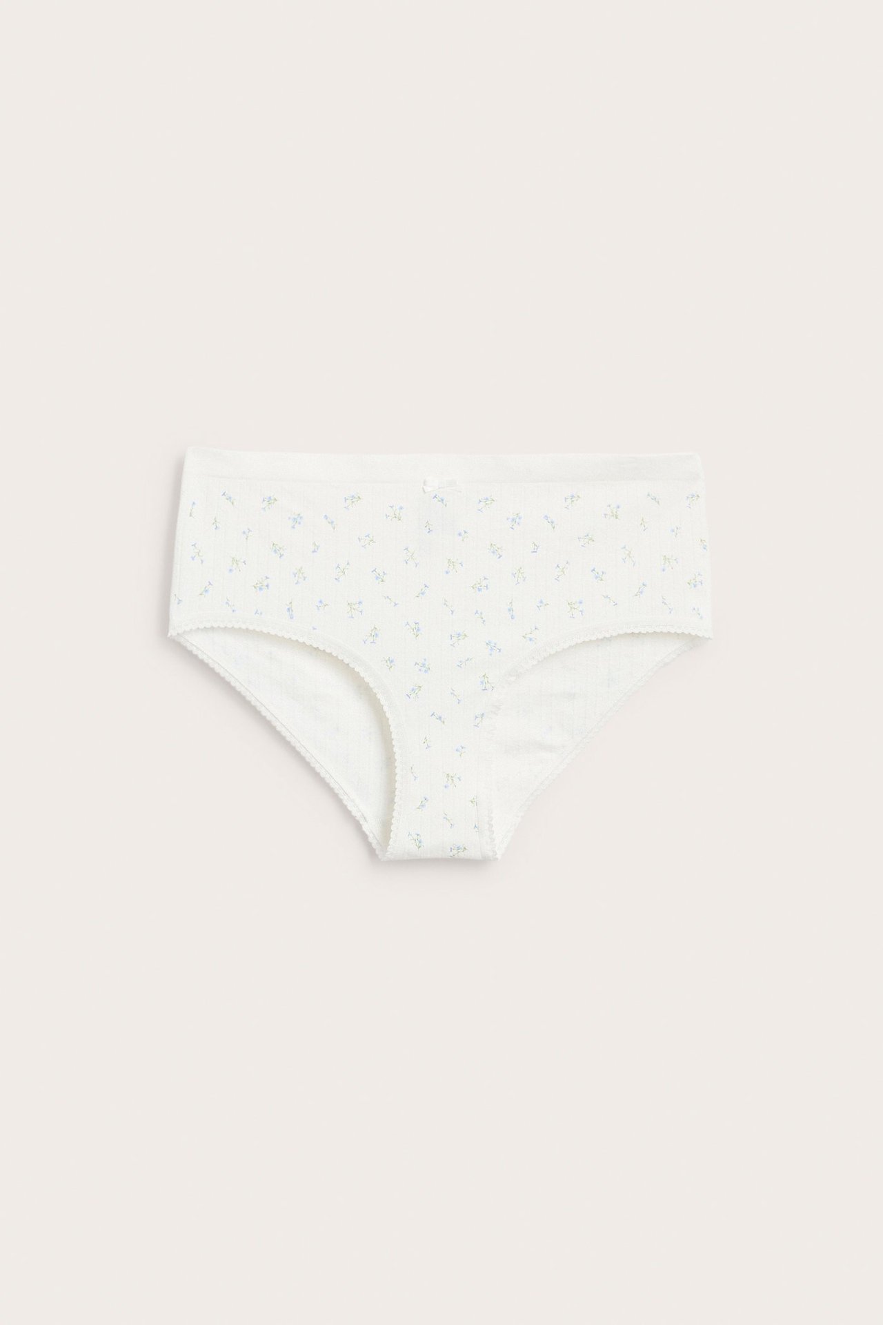 Frontvisning av hvit sømløs hipster-truse med diskret blomstermønster, pointelle-textur og picot-kanter.