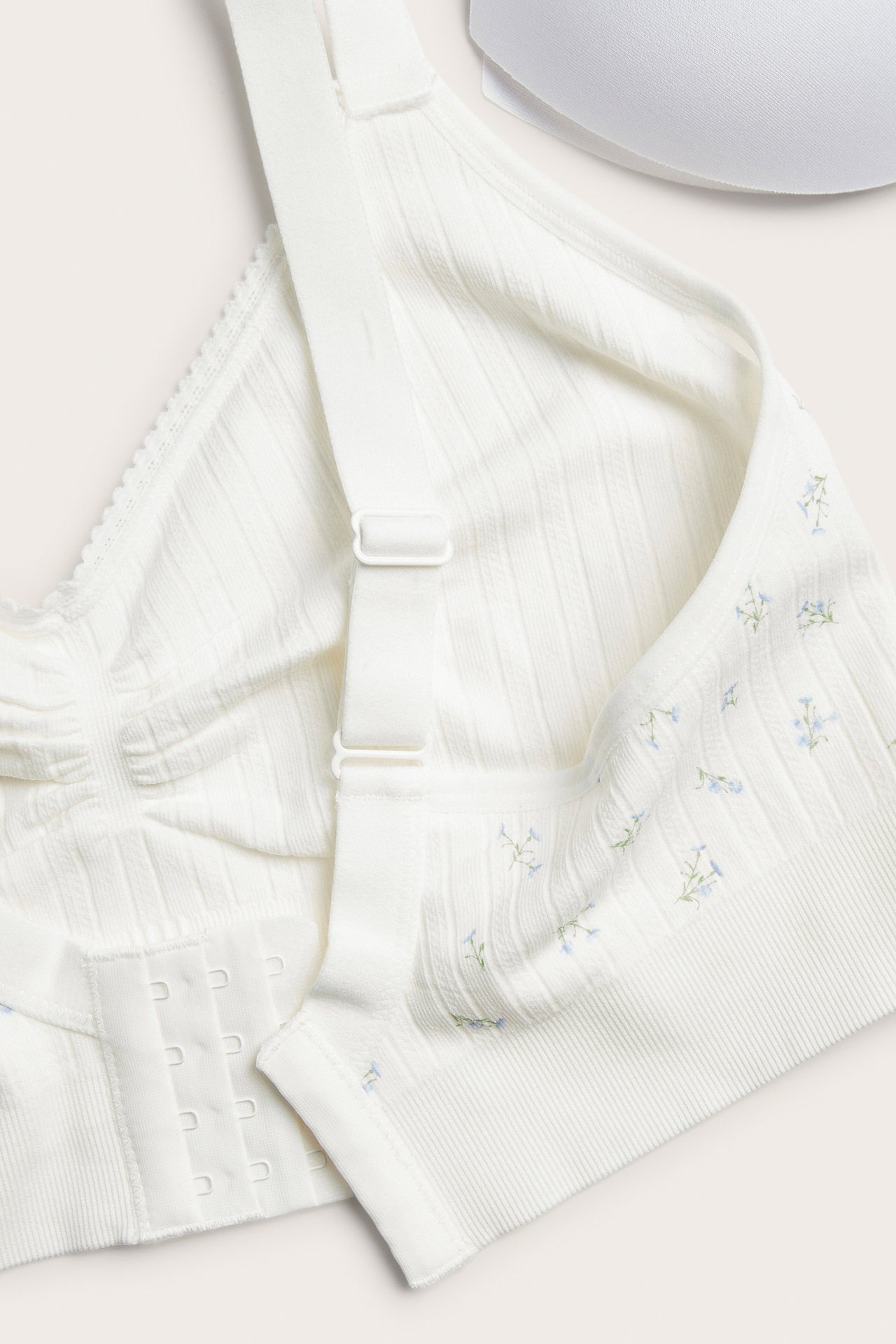 Närbild på en vit pointelle sömlös bh med ljusblått blommigt mönster och 4-radig hakknäppning.