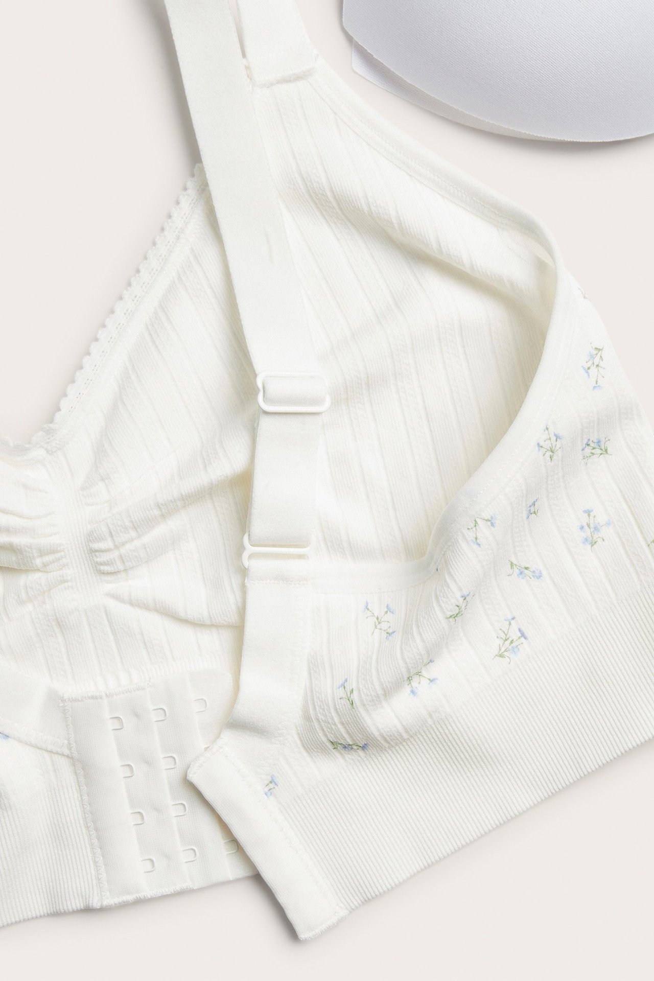 Närbild på en vit pointelle sömlös bh med ljusblått blommigt mönster och 4-radig hakknäppning.