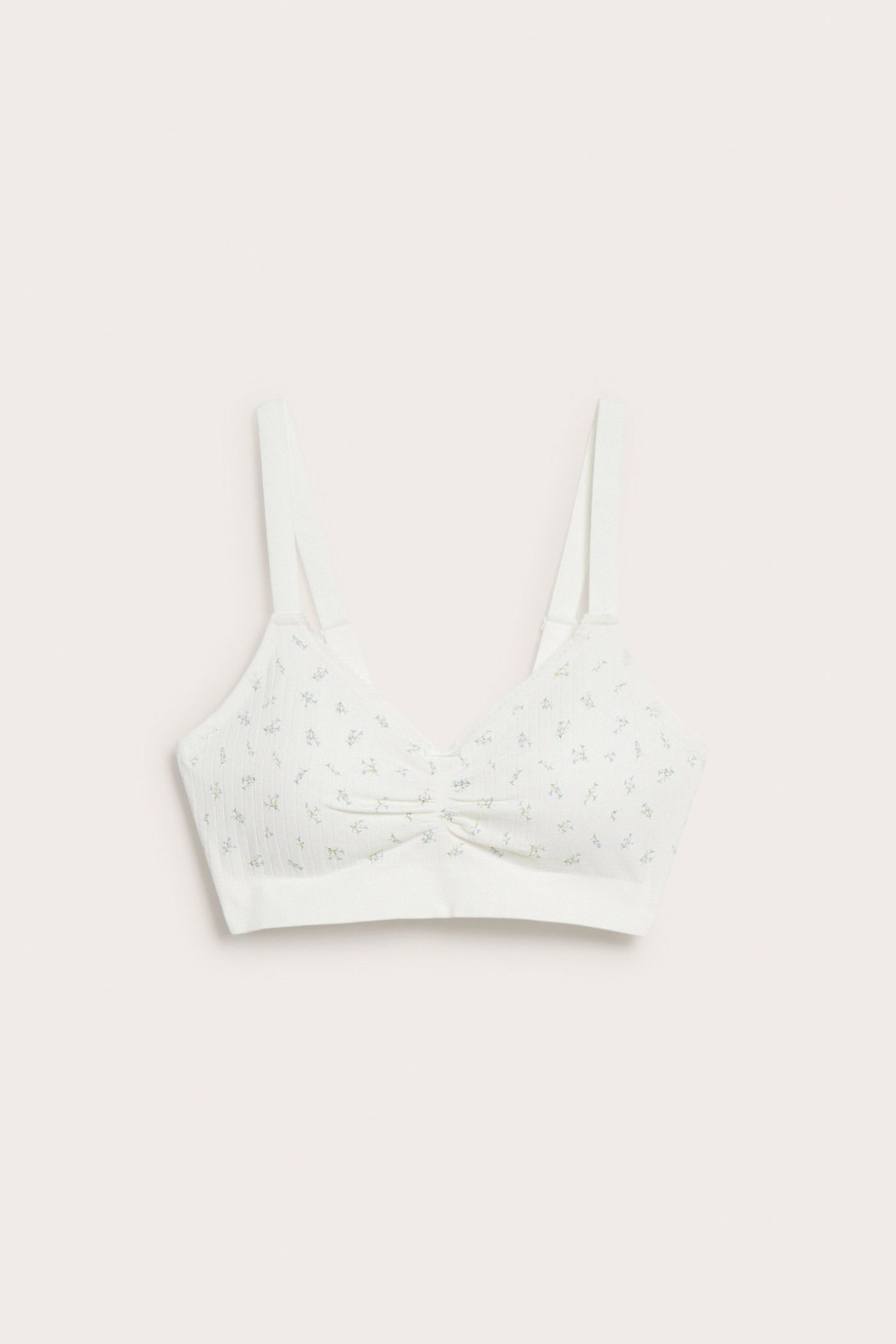 Framifrån: vit texturerad sömlös BH med diskret blommigt mönster och rynkad front.